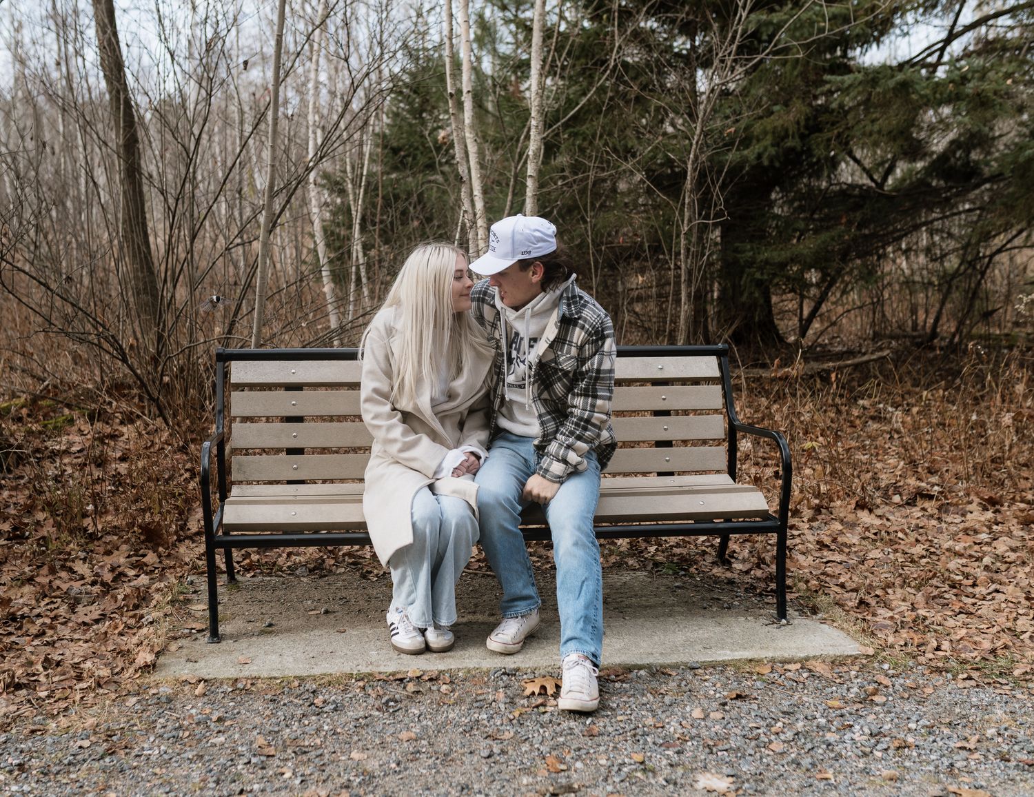 Young couple sitting close together on a park bench surrounded by fall foliage.
