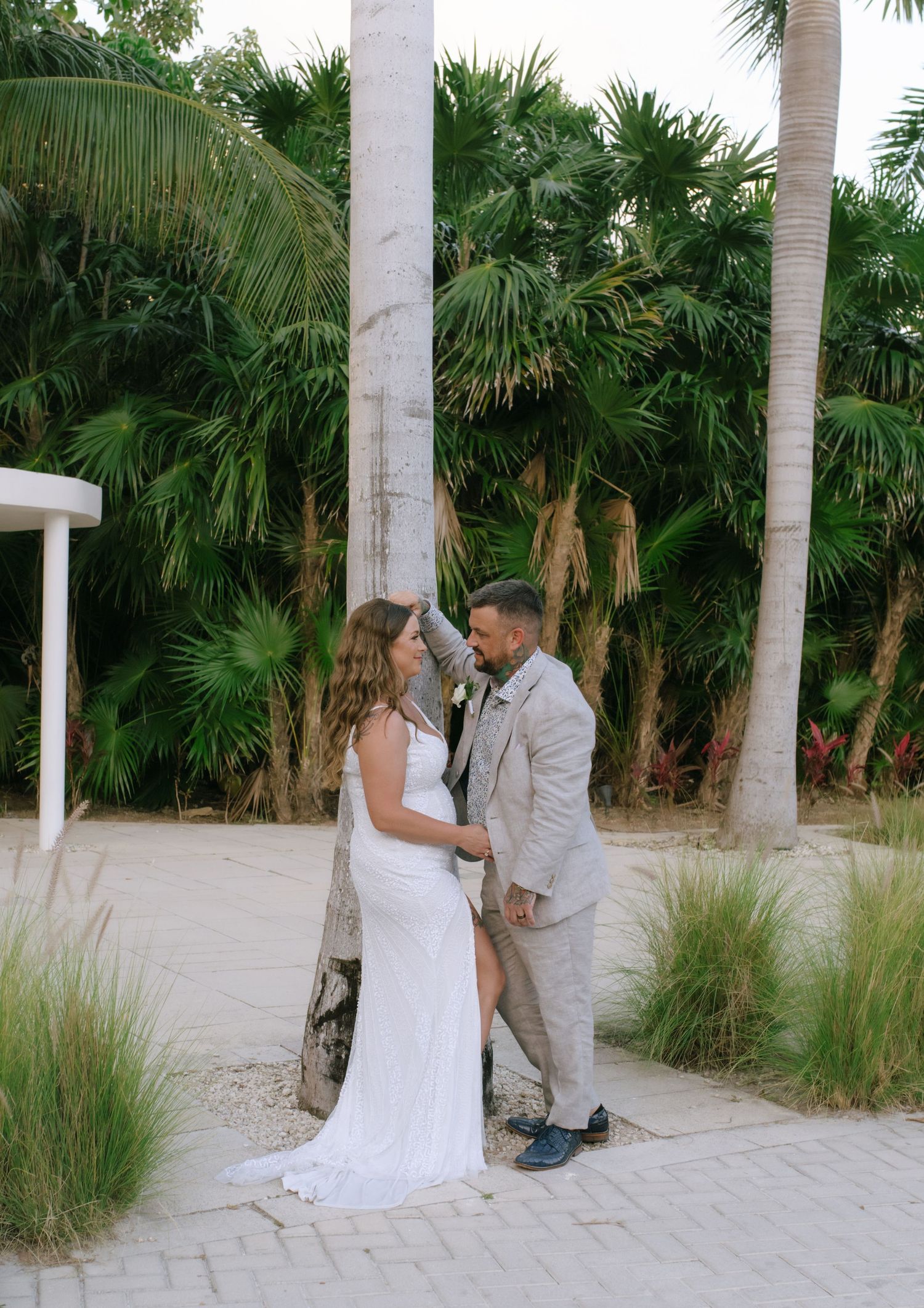 Bride and groom share a romantic moment surrounded by tropical palms at an outdoor beach wedding ceremony.