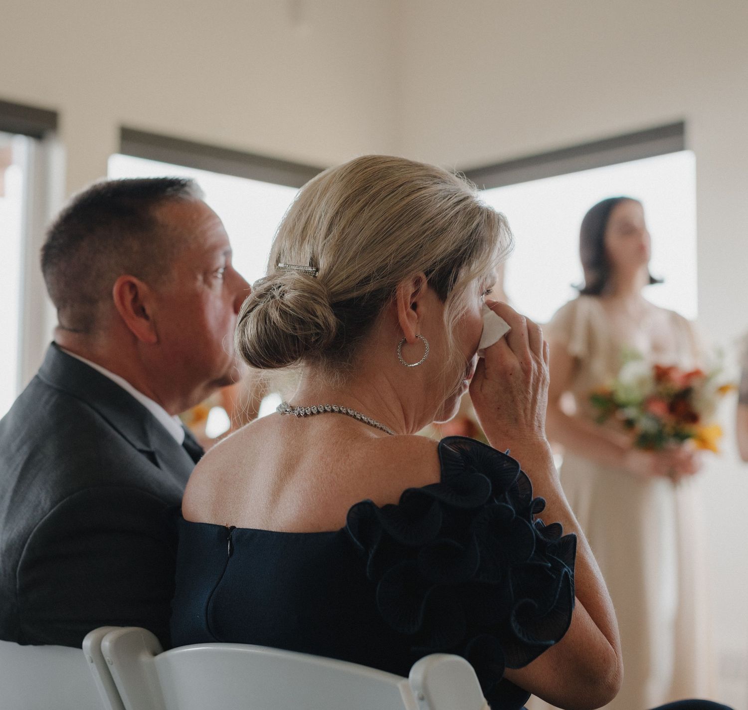Emotional wedding ceremony moment showing guests seated in white chairs indoors.