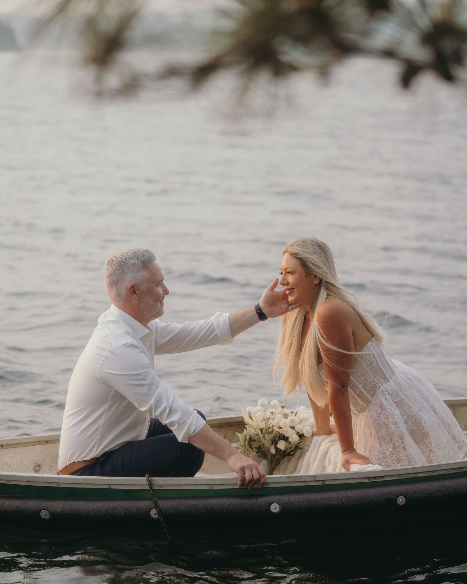 Couple in wedding attire sharing a romantic moment on a small boat on calm water, bride holding a bouquet.