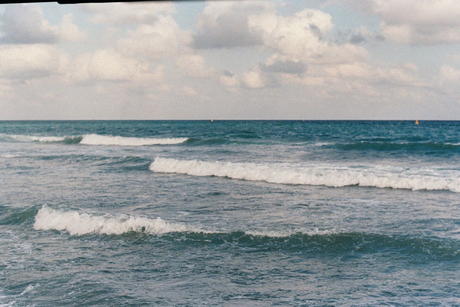 Rolling ocean waves crash against the shore under a cloudy sky.