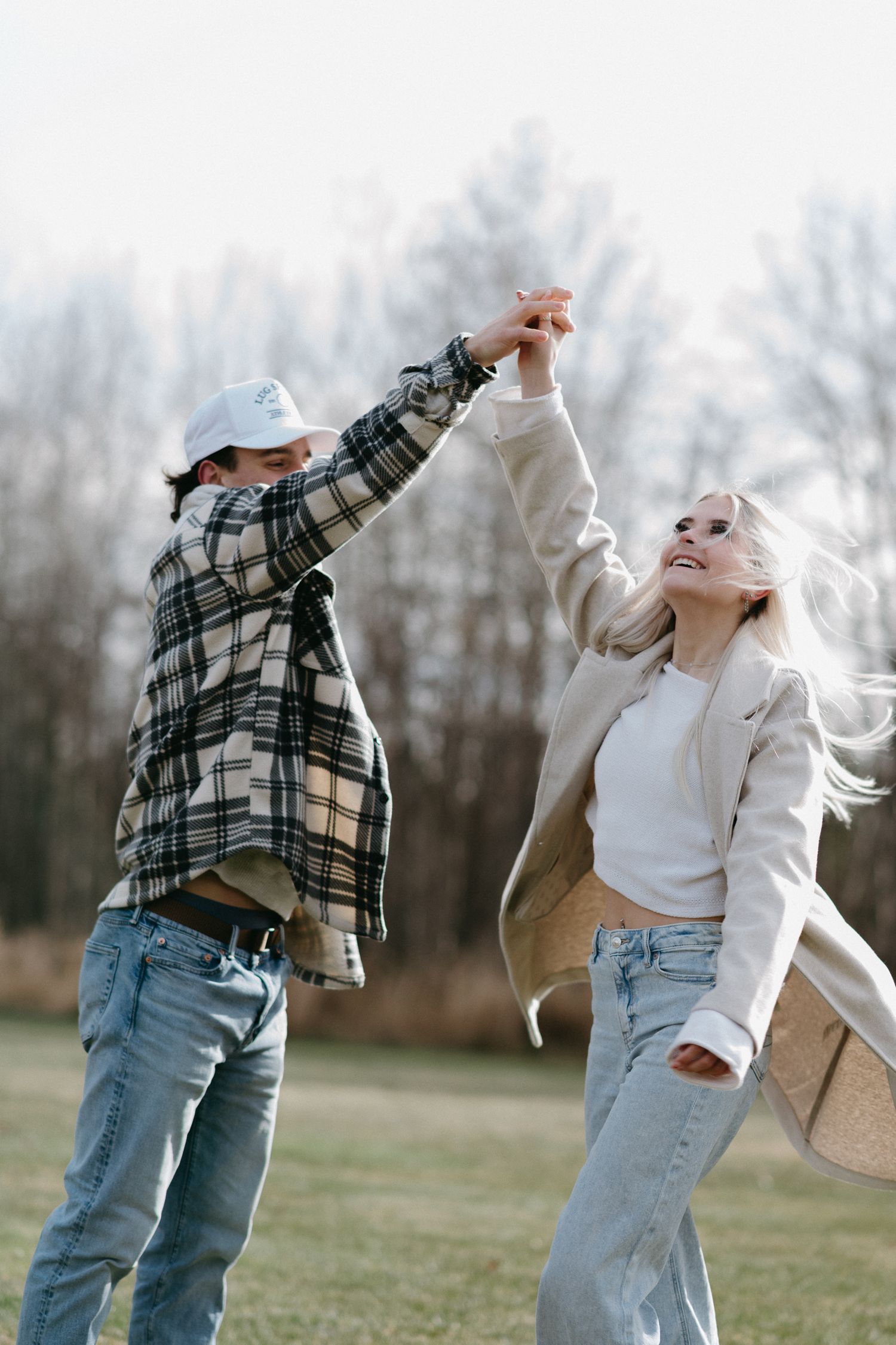 Happy couple dancing and holding hands in an open field with bare trees in background.