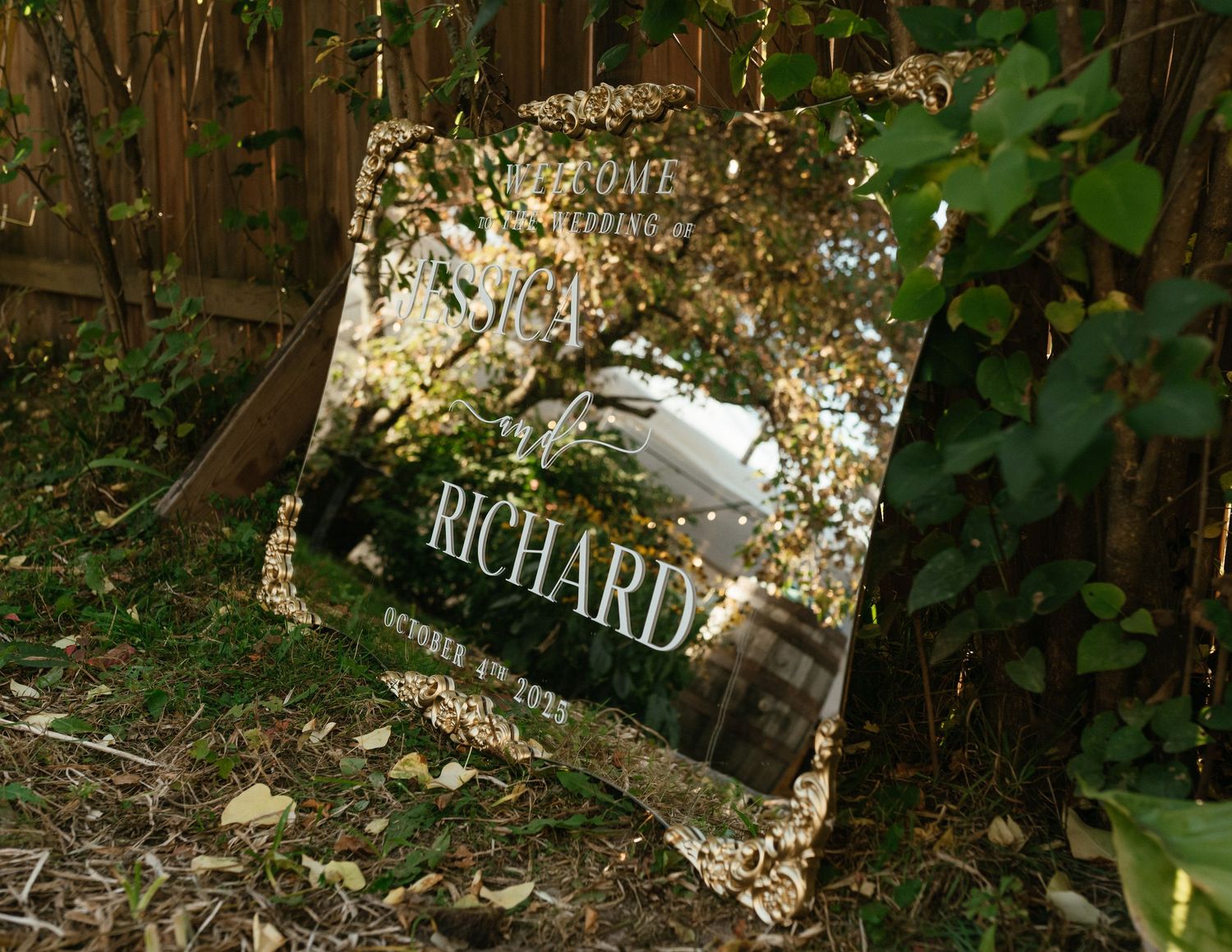 Mirrored wedding sign reflecting trees and foliage in an outdoor garden setting.
