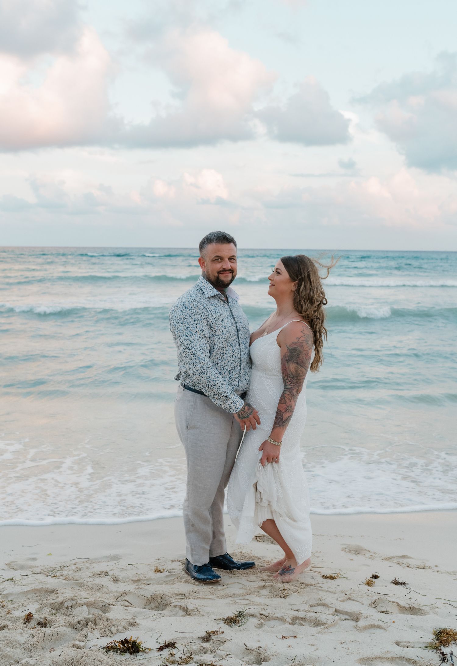 A couple shares a romantic moment on a sandy beach at sunset with gentle waves rolling in the background.