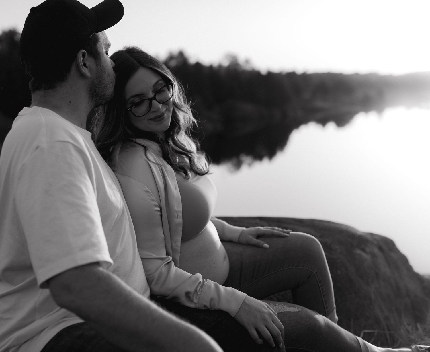 A couple sits together in an intimate outdoor setting during a maternity photoshoot.