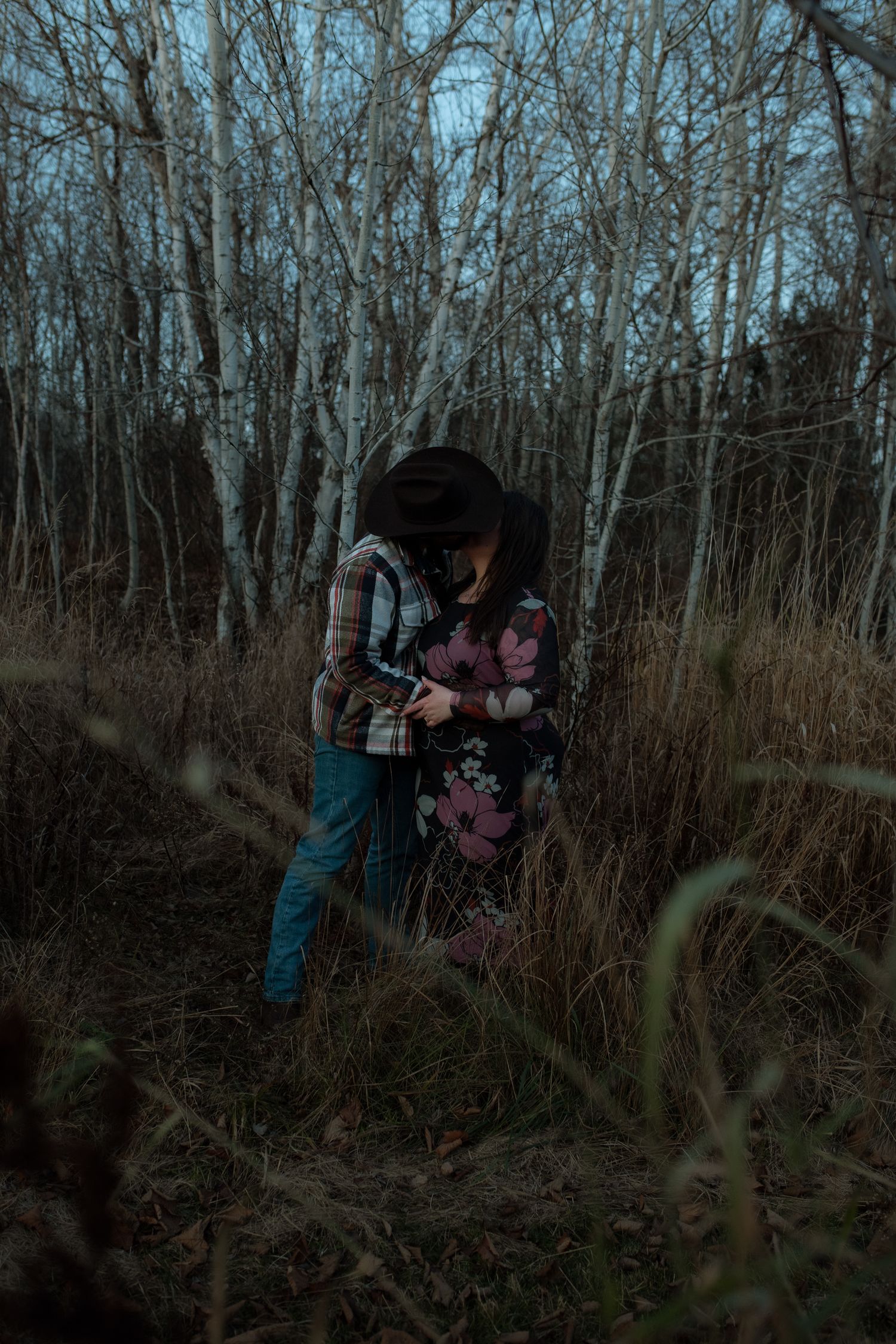 People explore a dense wooded area with bare trees on a cloudy winter day.