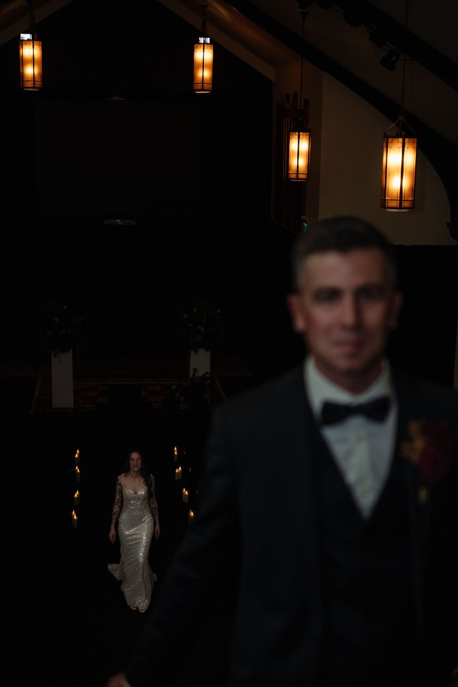 Bride walks toward groom in dimly lit wedding venue with warm hanging lanterns creating romantic atmosphere.