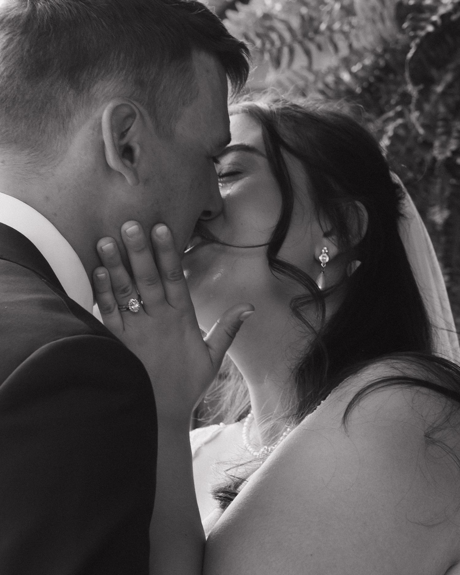 Black and white wedding photo of bride and groom sharing a romantic kiss, bride wearing veil and pearl earrings.