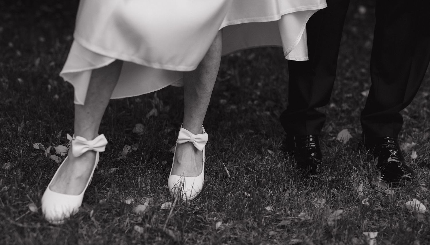 Close-up of wedding dress hem and shoes on dark ground.