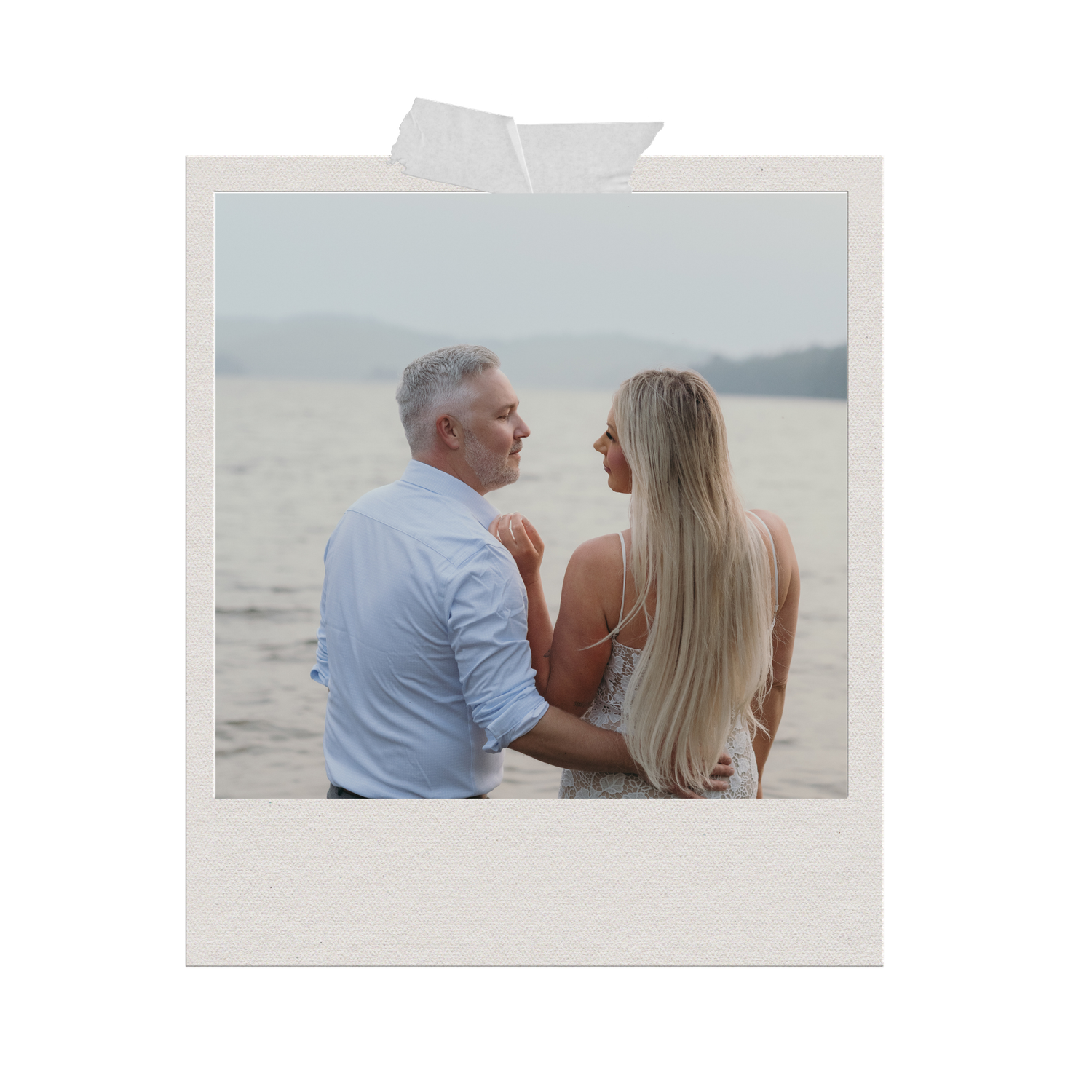 A couple sits together by a serene lake, the woman with long blonde hair and the man in a light blue shirt.