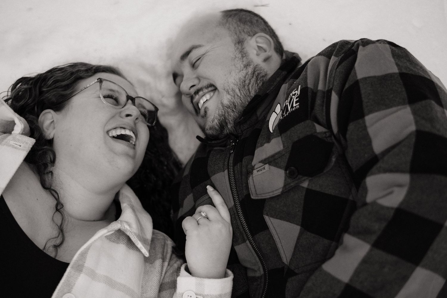 Black and white photo of a laughing couple lying on the ground, sharing a joyful moment together.