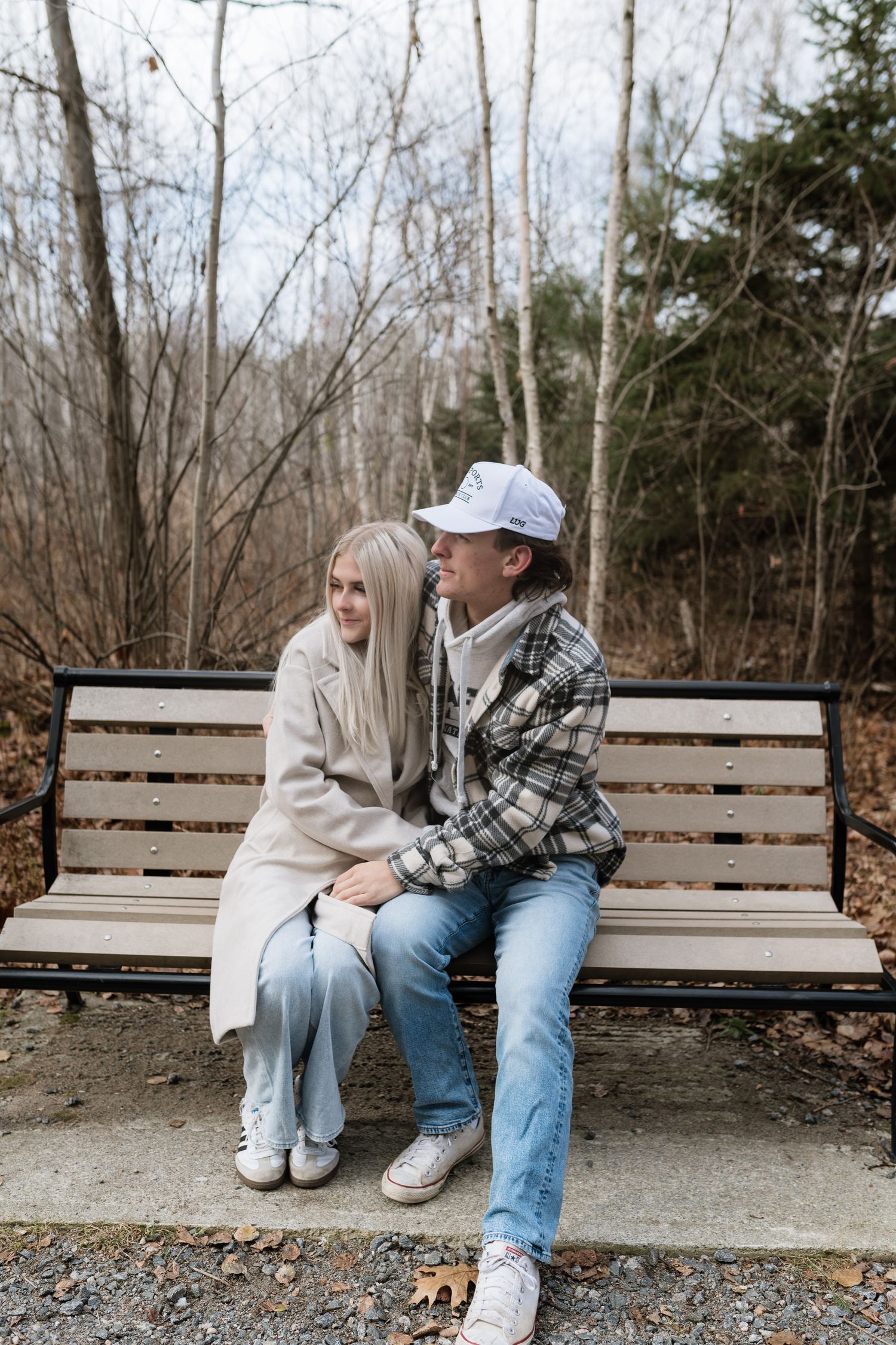 Young couple sitting close together on park bench surrounded by bare autumn trees.