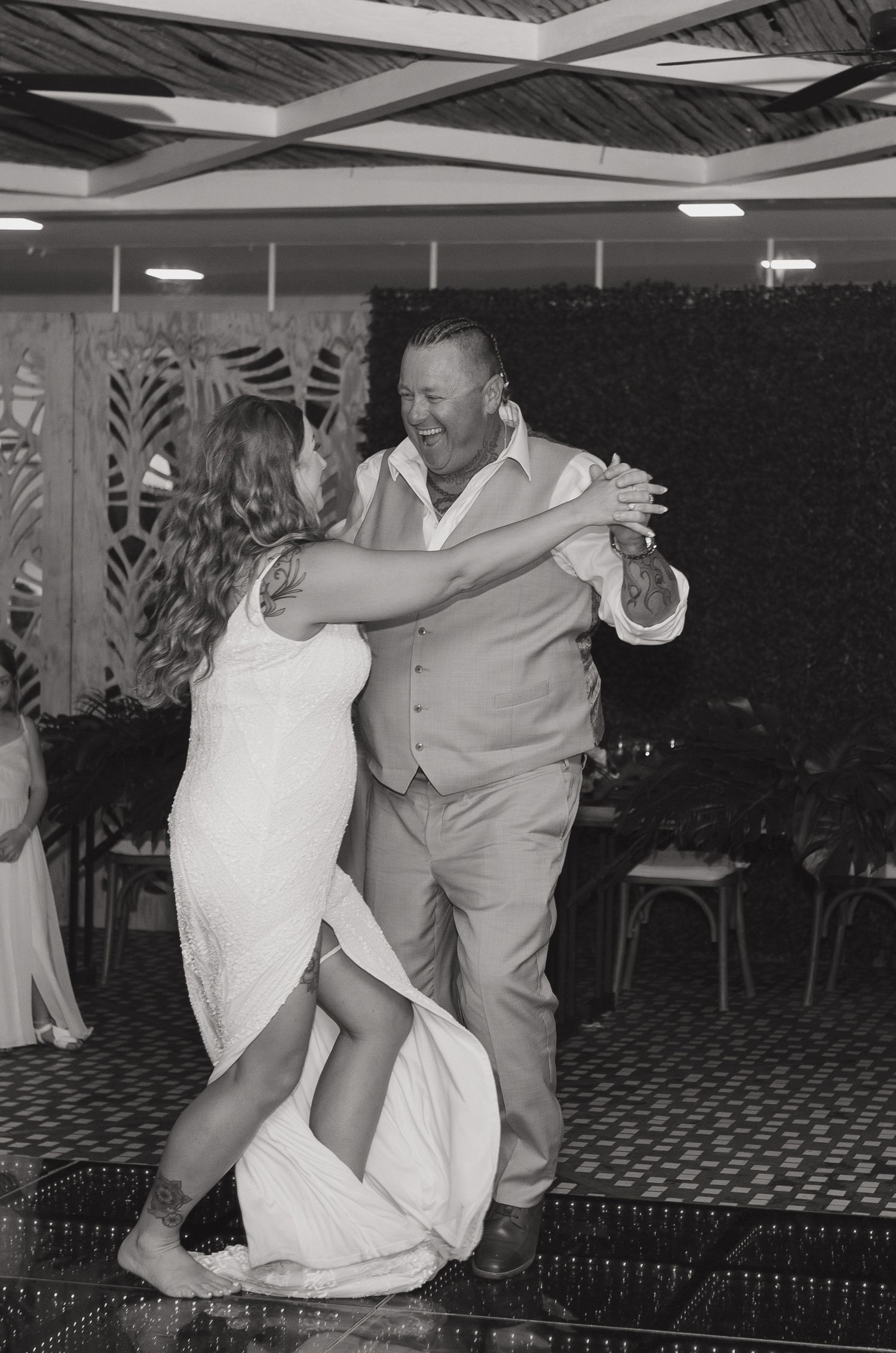 A couple dances together at an indoor event venue with a patterned carpet and ceiling lights.