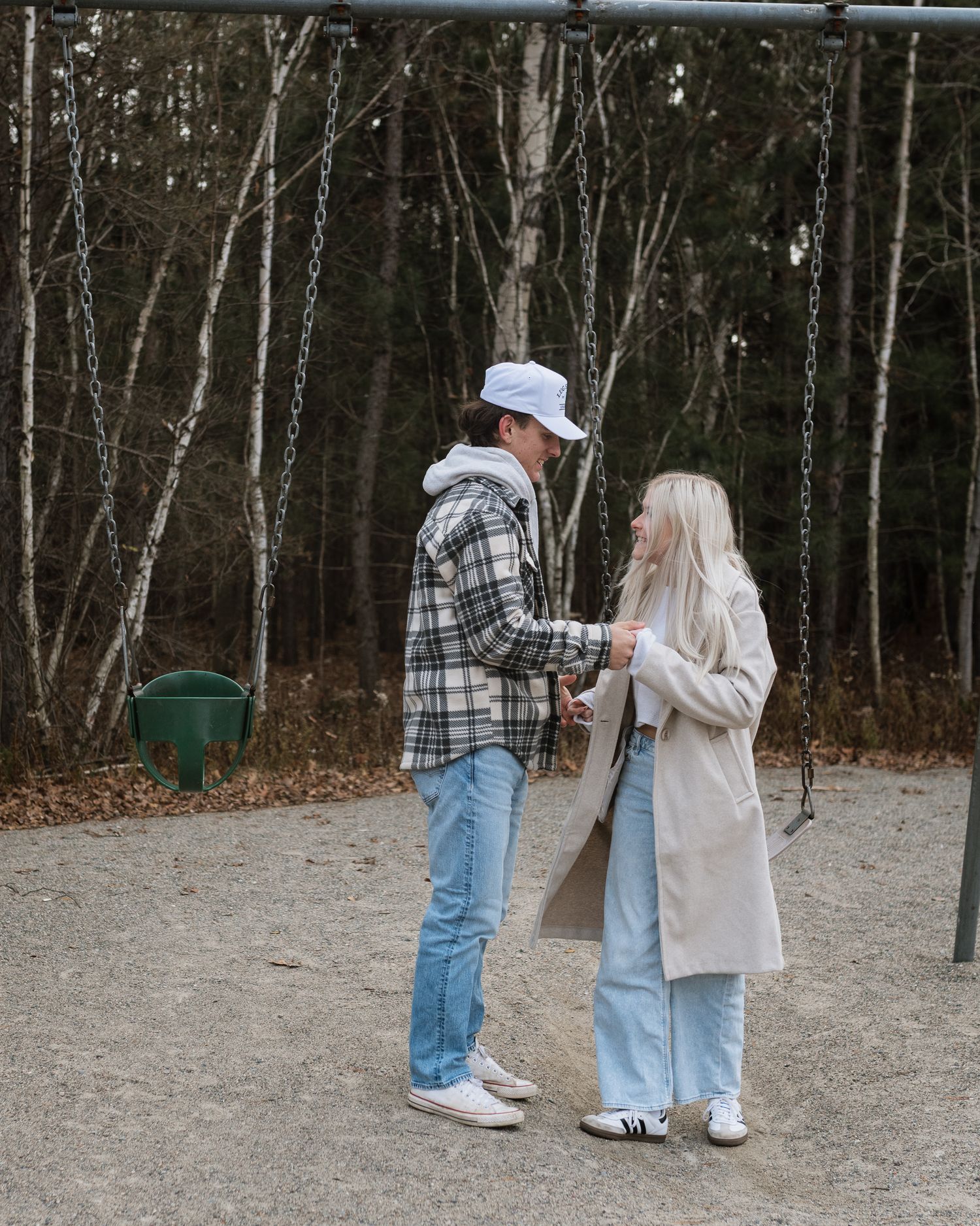 Young couple holding hands at playground near swings, surrounded by bare autumn trees.