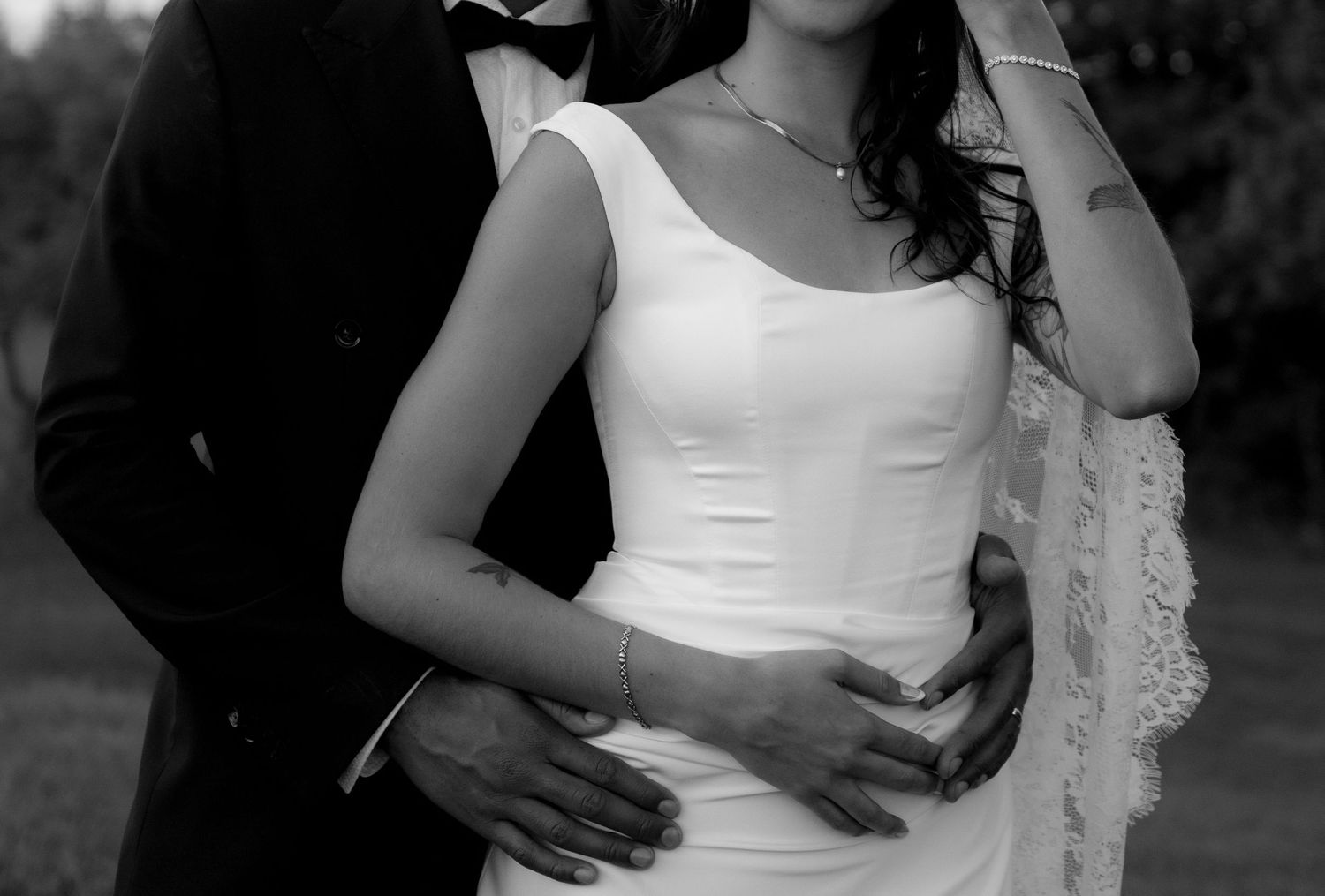Black and white photo of a bride in white gown and groom in tuxedo embracing outdoors on their wedding day.