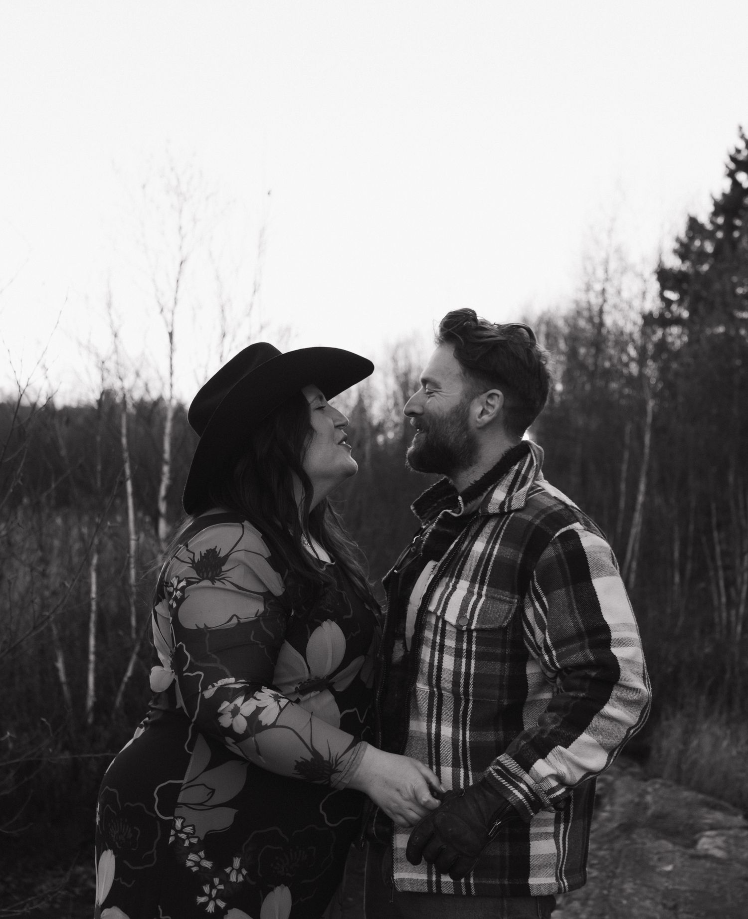 A couple in plaid winter clothing share a romantic moment in a snowy wooded setting during winter.
