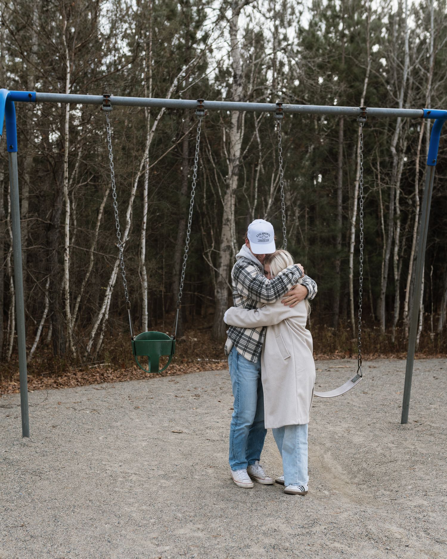 Couple embracing at a playground swing set with tall birch trees in the background.