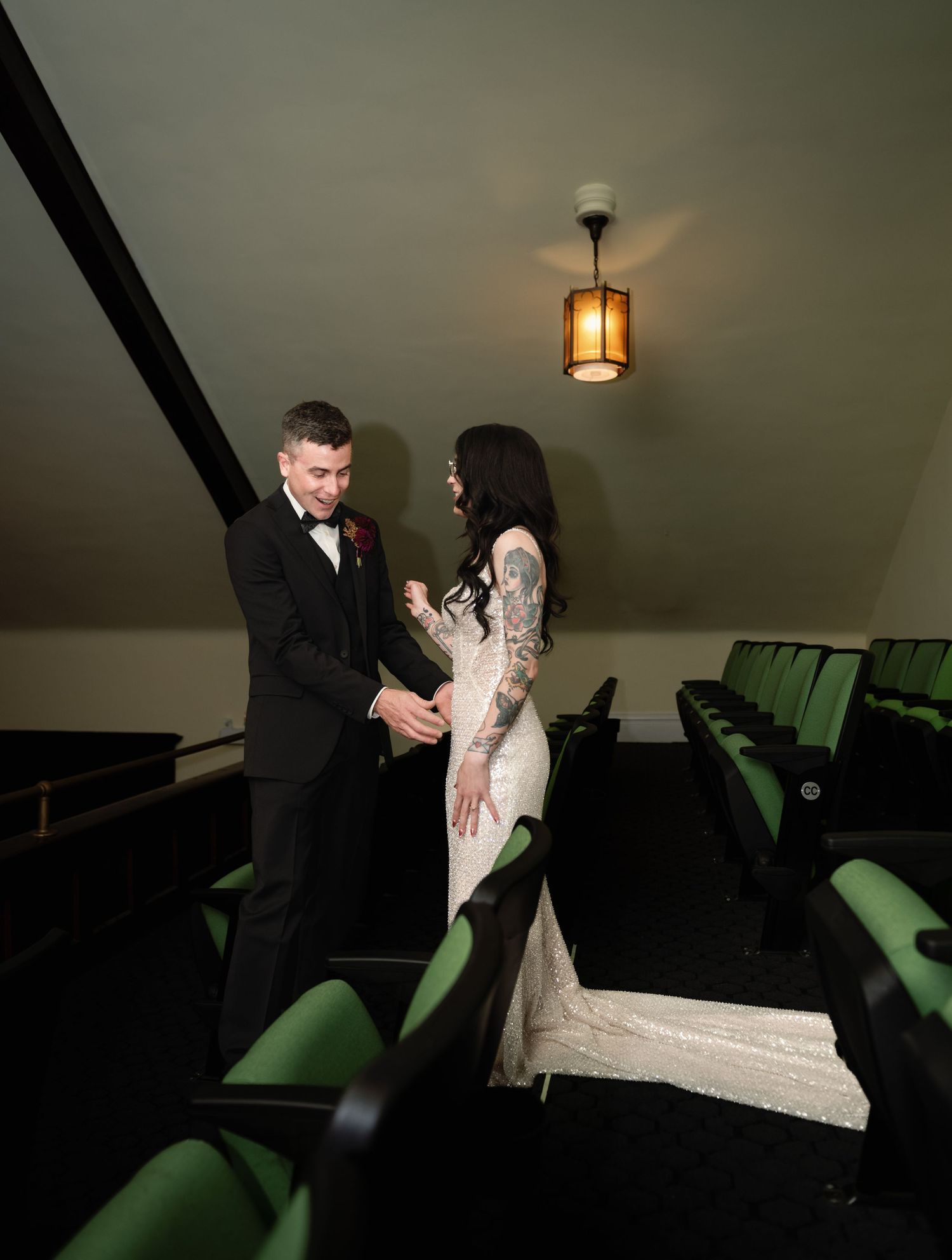 Bride and groom share a romantic moment in a vintage theater with green seats and warm lighting.