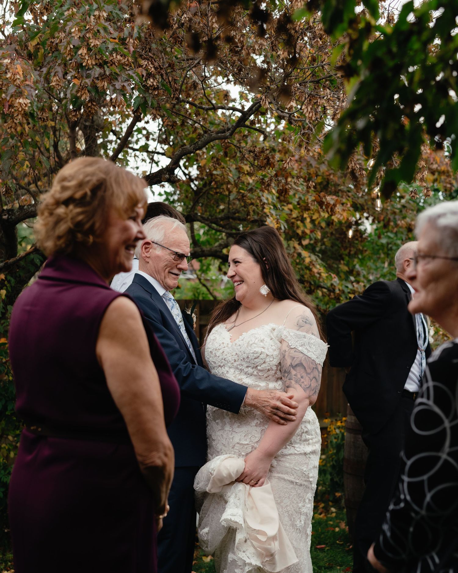 Wedding celebration with guests gathered outdoors among autumn trees.