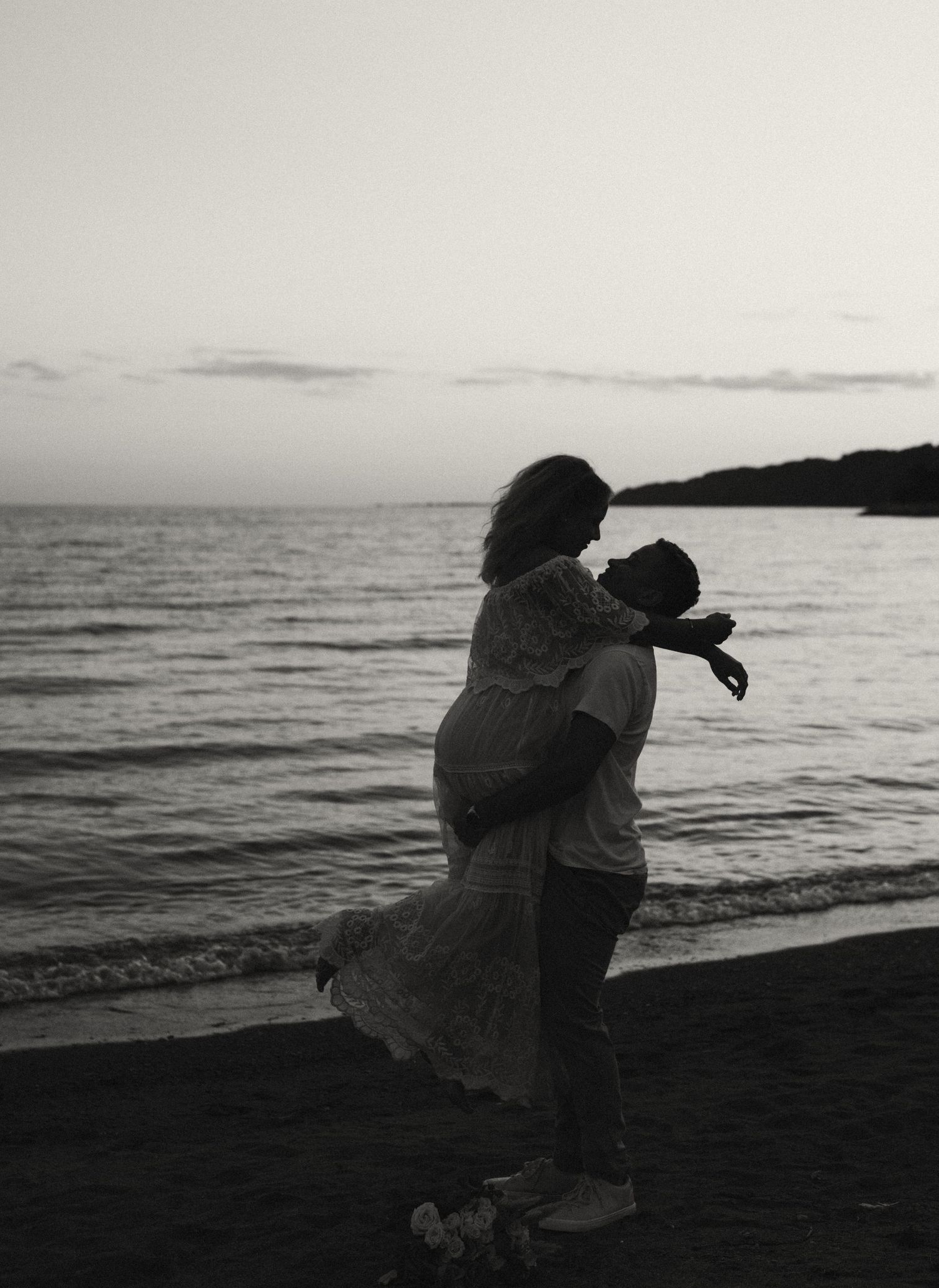 A silhouetted couple shares a joyful embrace on the beach at sunset.
