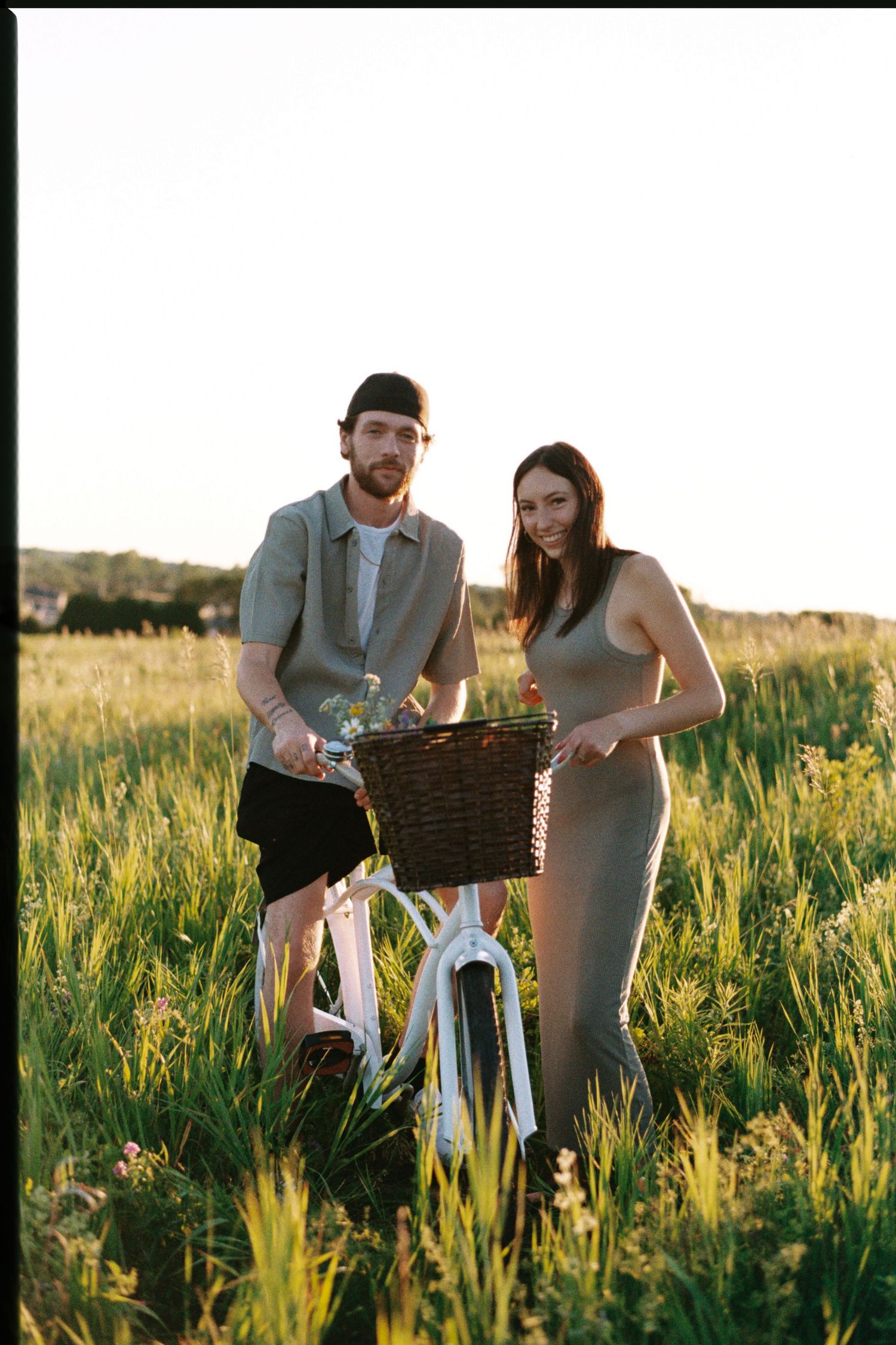 A couple explores a vintage camera together in a sunlit meadow during golden hour.