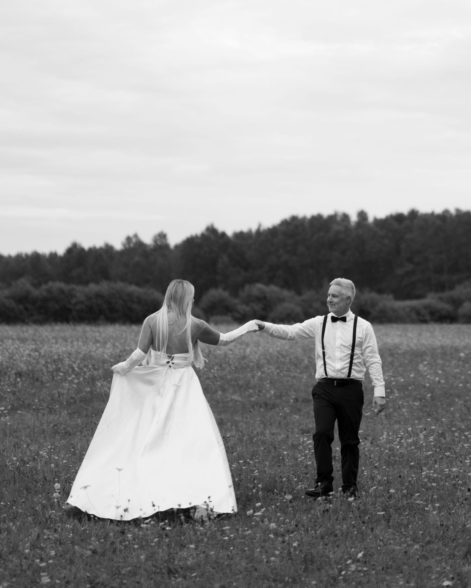 Black and white photo of couple in formal wear dancing in wildflower field.