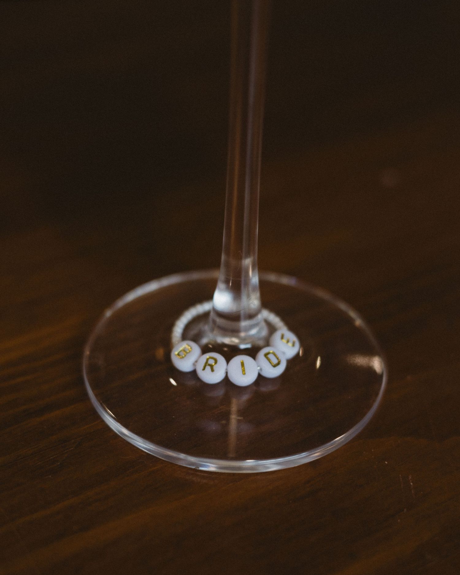 Close-up of a wine glass stem with decorative bride charm on wooden surface.