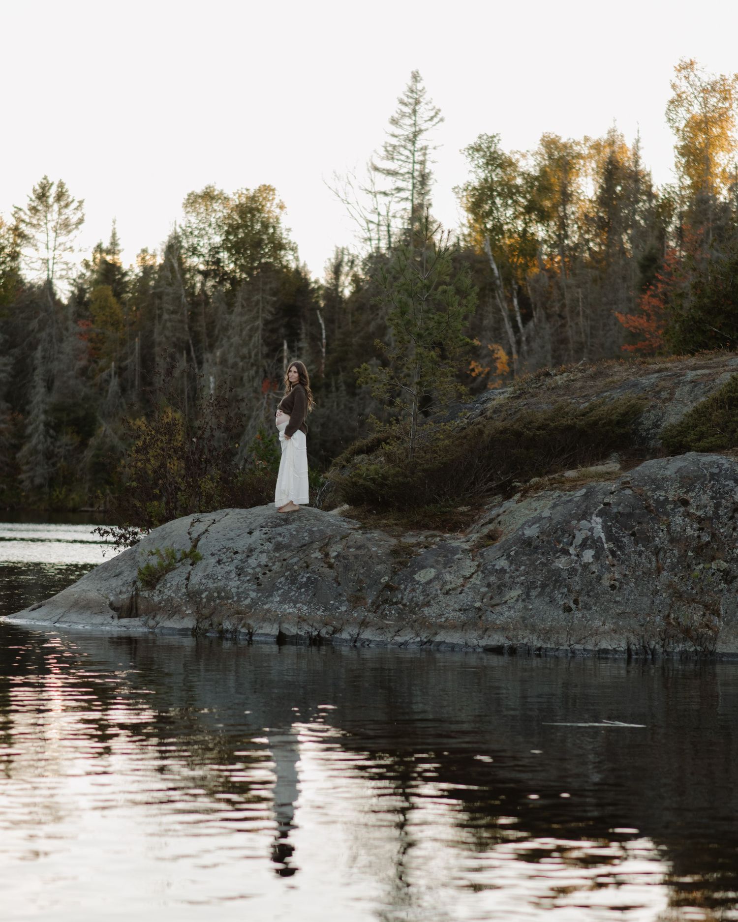 A serene lakeside scene with rocky cliffs and evergreen trees at sunset, reflecting on calm waters.