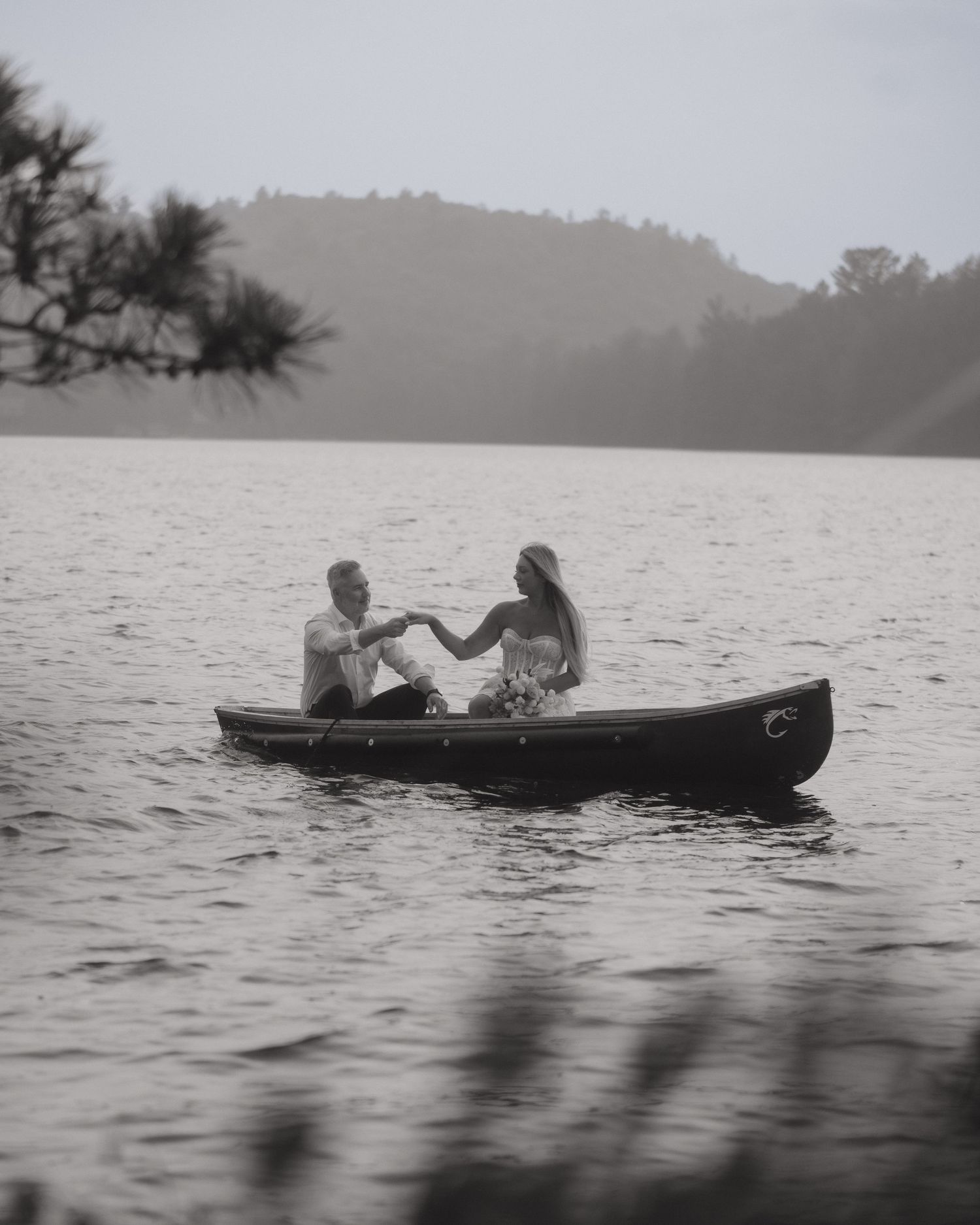 Vintage black and white photograph showing people relaxing on canoes in a misty lake on a summer day.