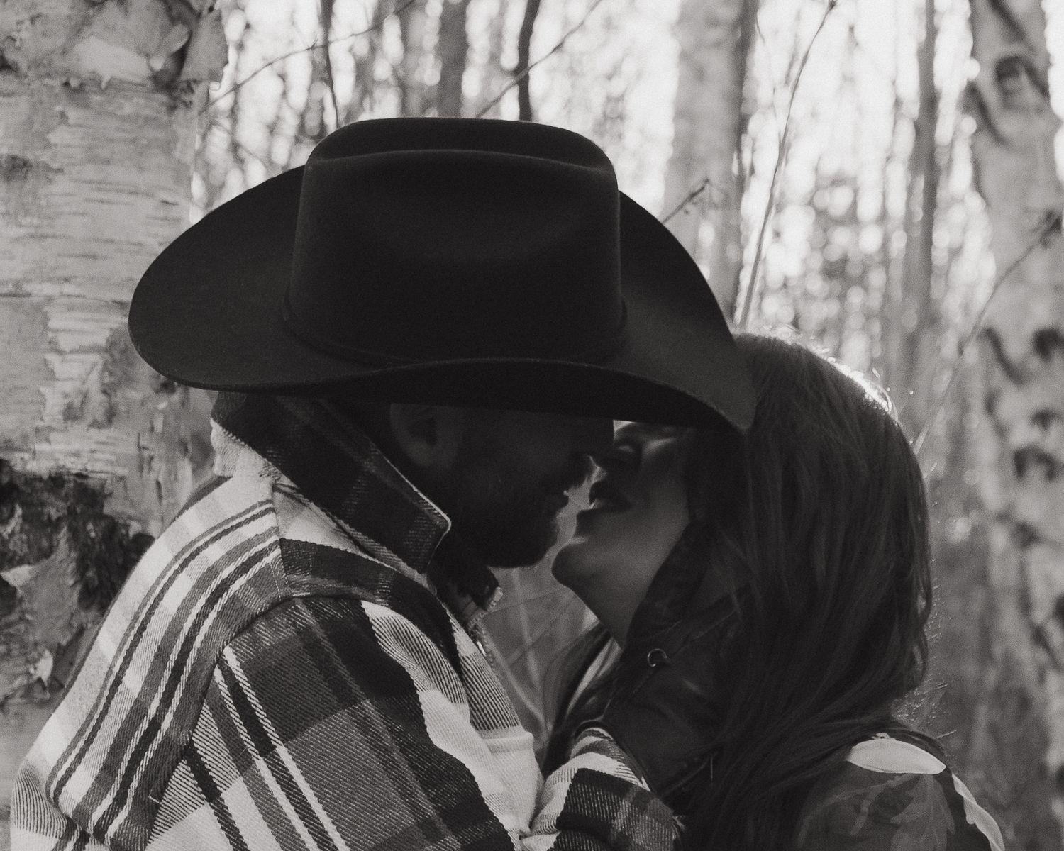 A romantic black and white photograph of a couple kissing in a birch forest.