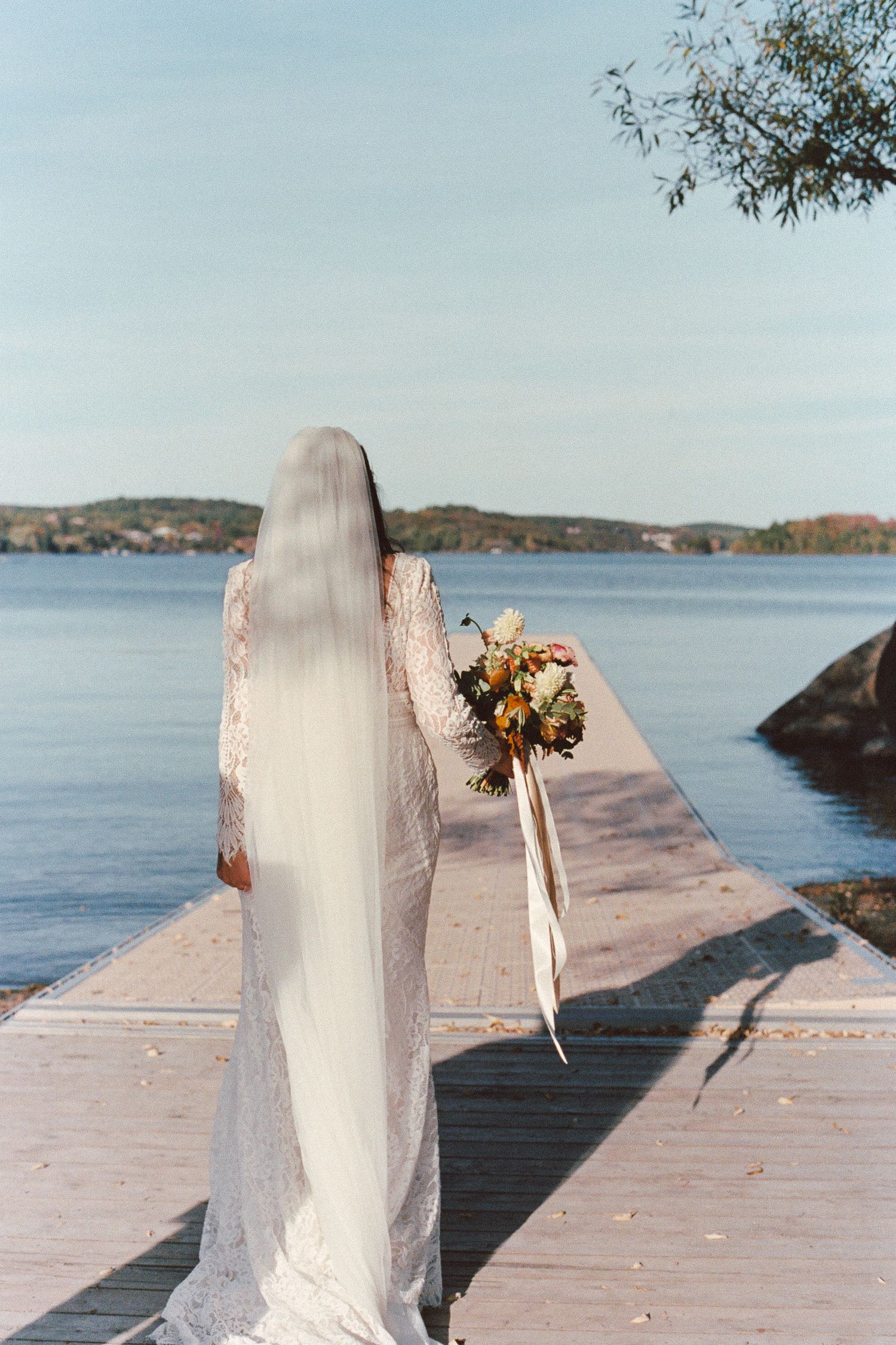 A rustic wooden dock stretches over calm blue water with dried flowers decorating white painted posts along its length.