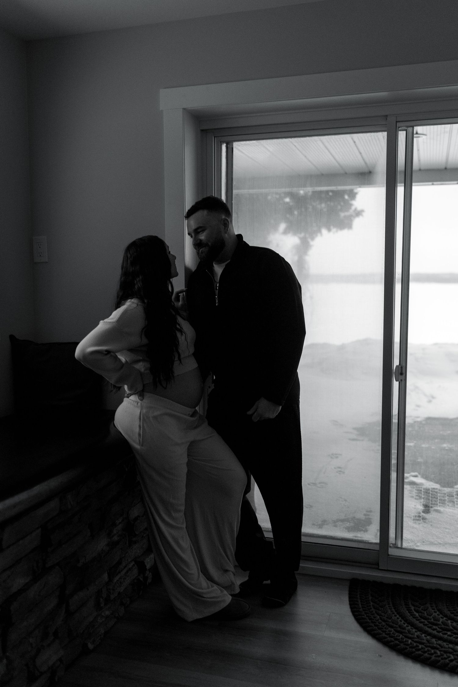 Black and white silhouette of couple standing by a large window in cozy interior.