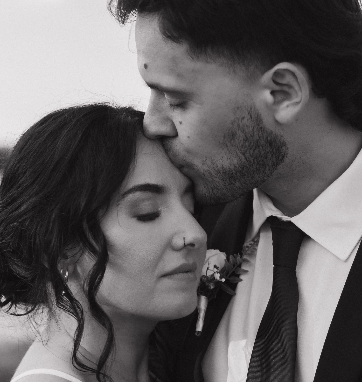 Black and white wedding photo of groom kissing bride on forehead, couple in formal attire, romantic and intimate moment.