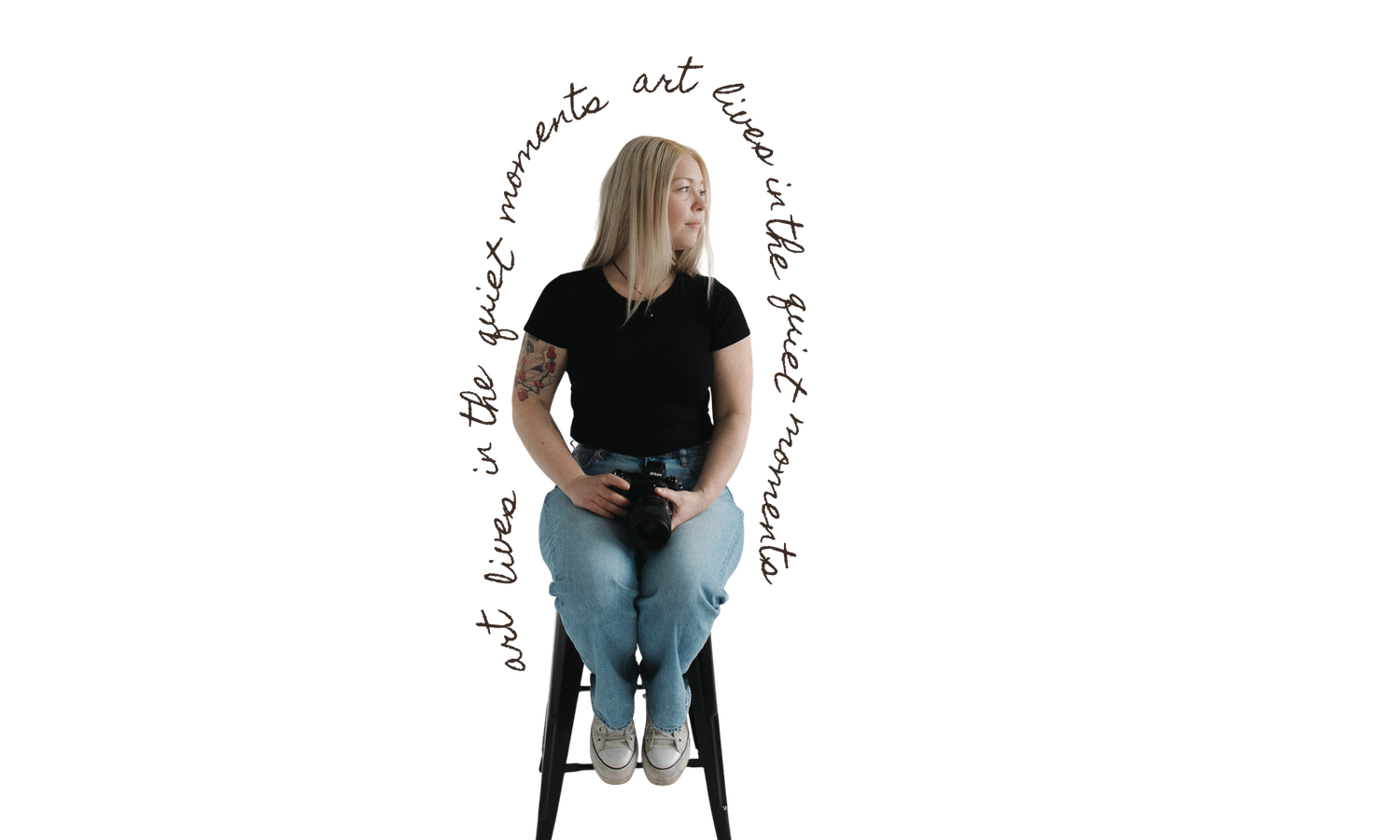 Woman in black t-shirt and jeans sitting on a stool surrounded by cursive text reading art lives in the quiet moments.