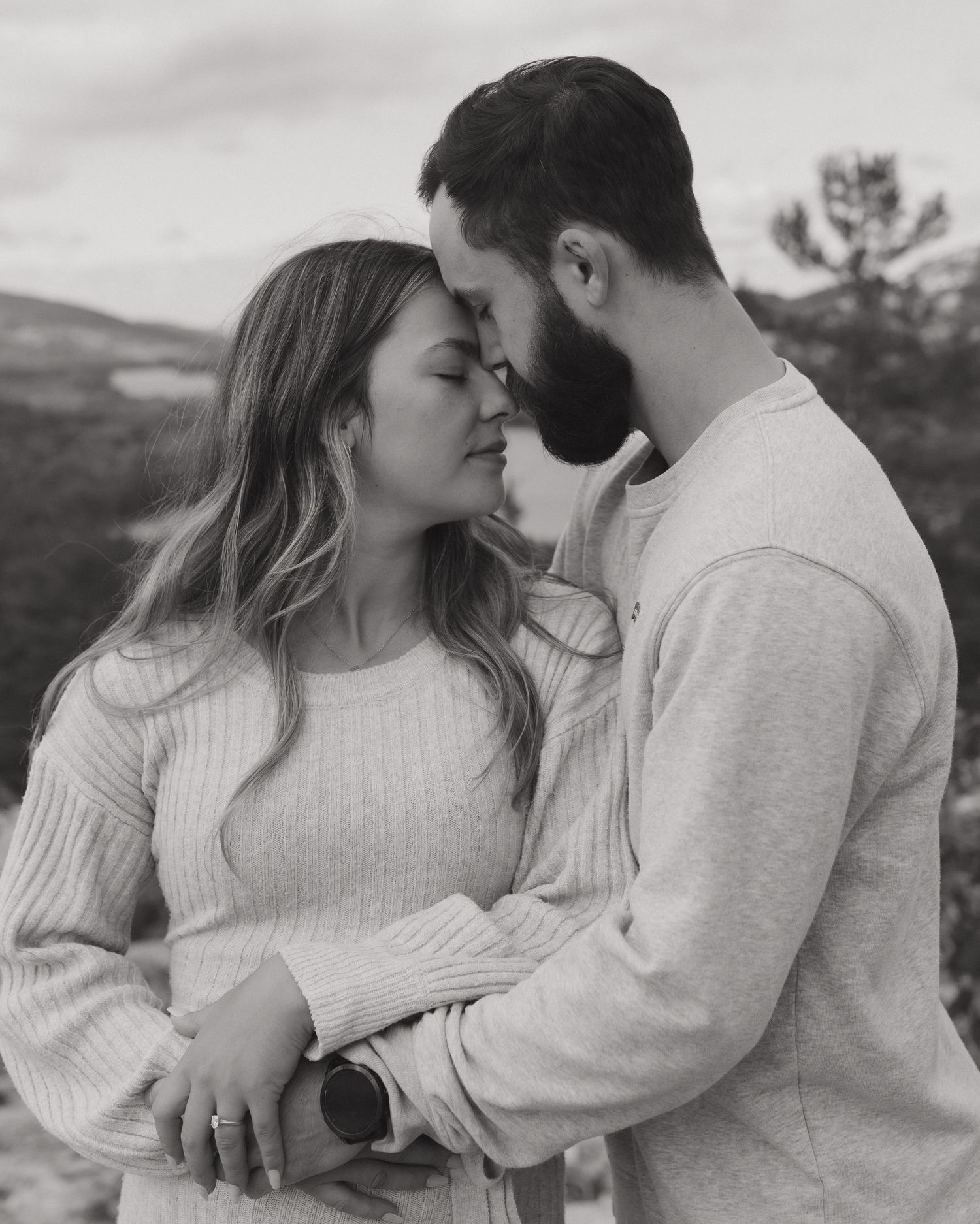 An intimate portrait of a couple in white sweaters embracing against a mountain backdrop.
