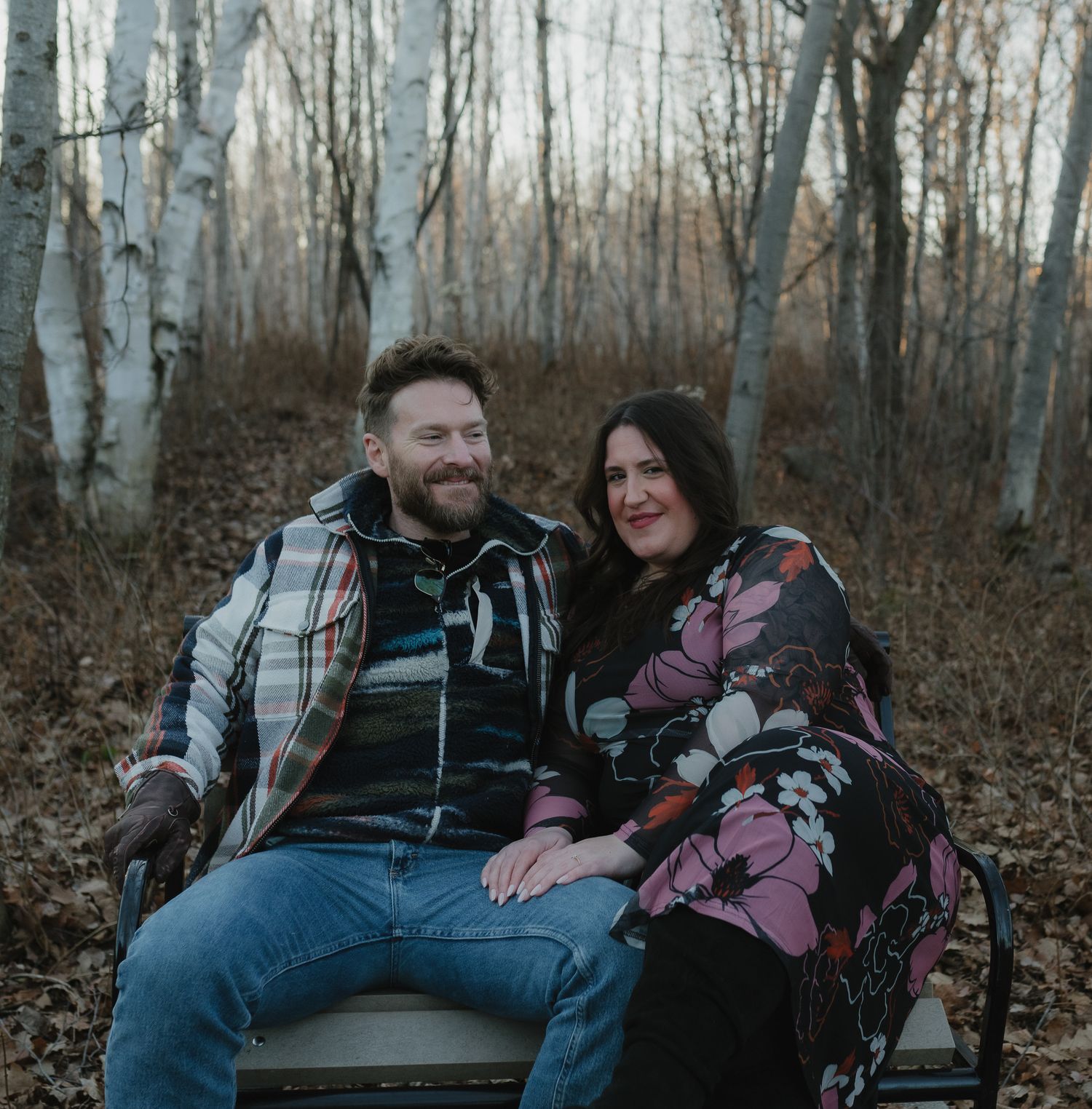 Couple sitting together in a wooded area with birch trees on a winter afternoon.