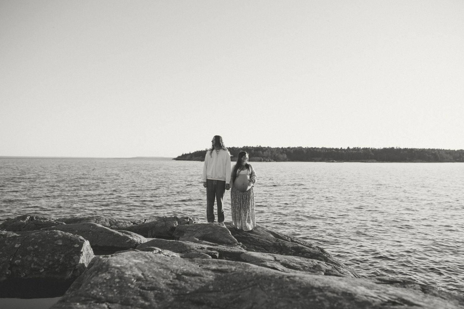 A couple standing on coastal rocks overlooking the ocean in black and white.