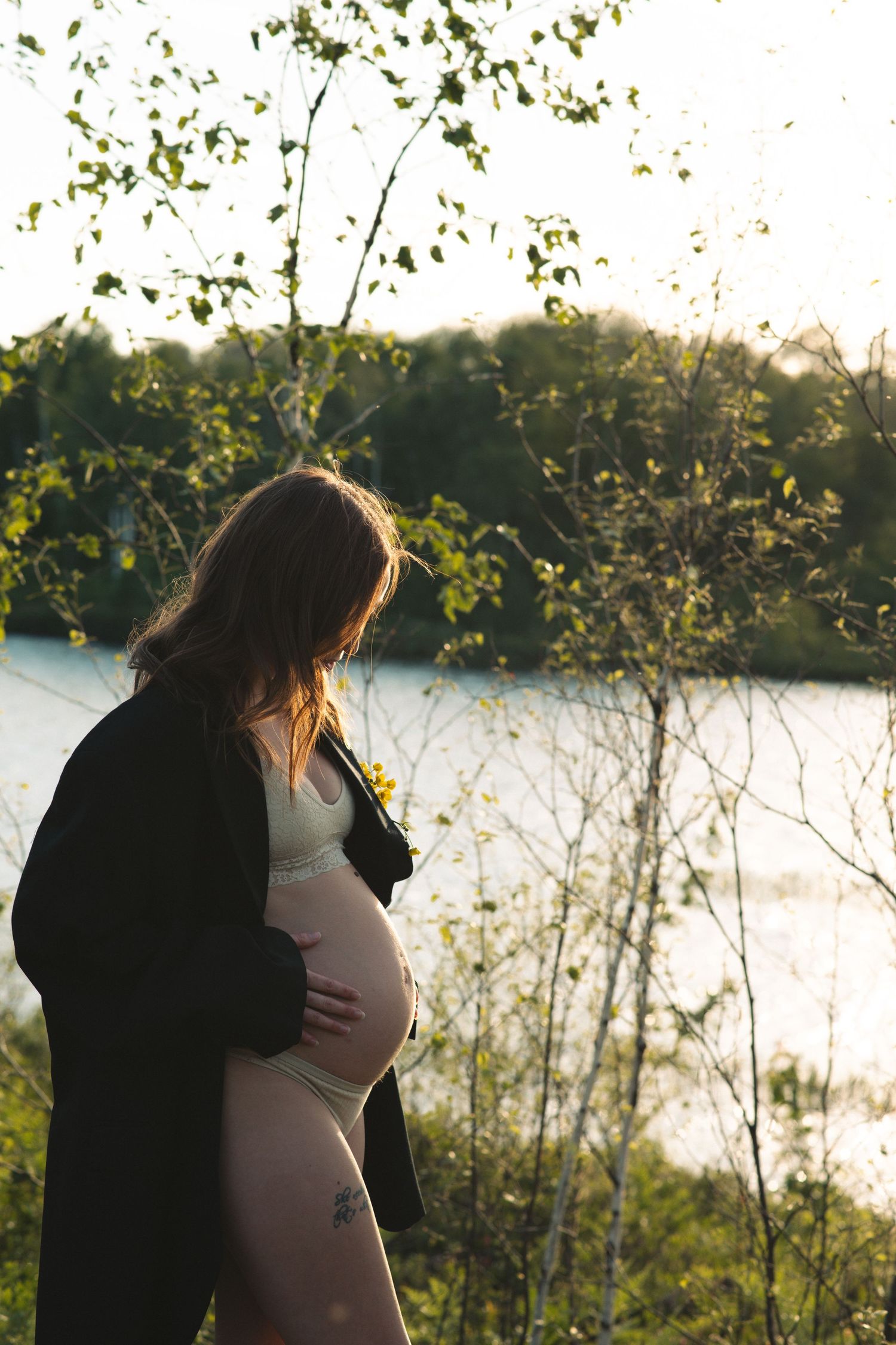 Silhouettes embrace by a lake during golden hour with trees in the background.