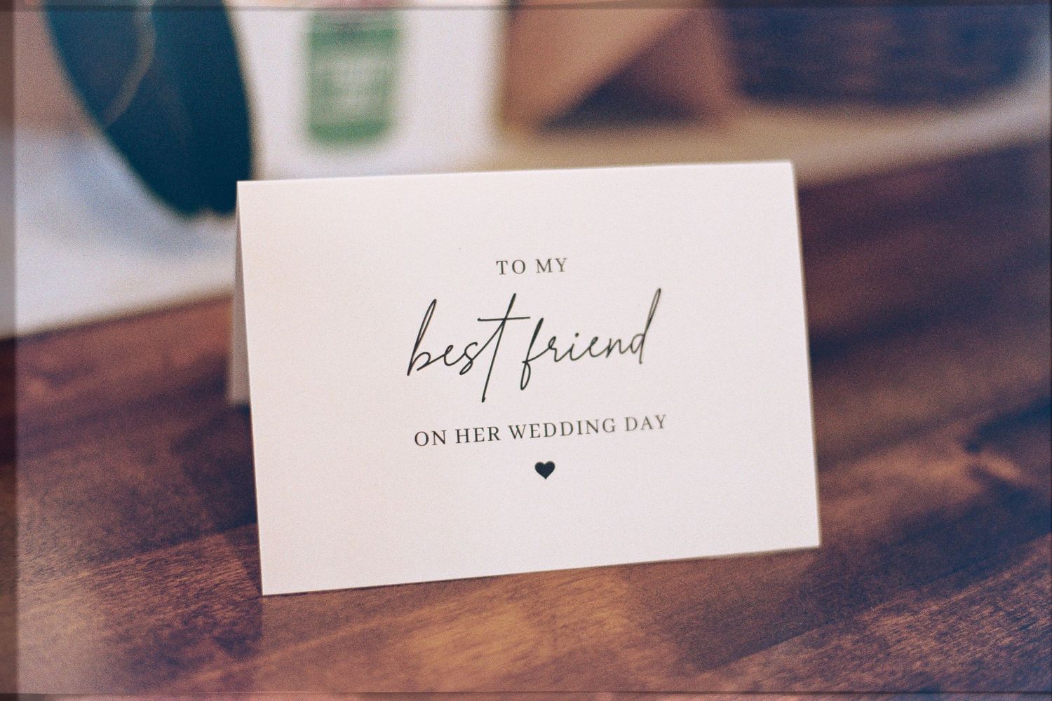 Elegant white wedding card reading 'To My Best Friend On Her Wedding Day' with heart, displayed on wooden surface.
