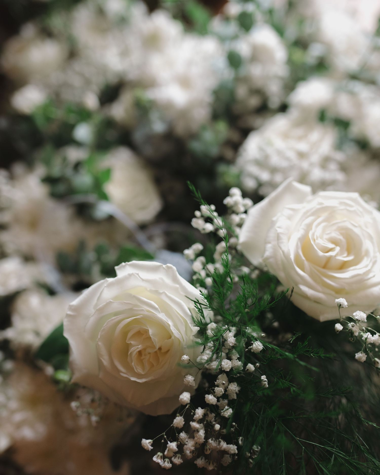 Close-up of elegant white roses and baby's breath arrangement with green foliage, perfect for weddings or events.