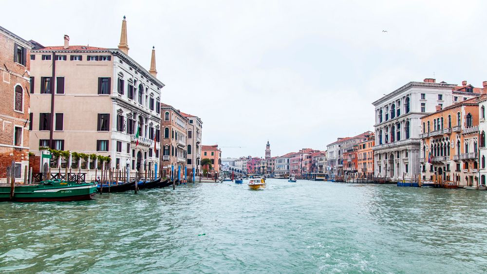 Historic Venice Grand Canal with colorful buildings, boats, and gondolas on calm waters under an overcast sky.