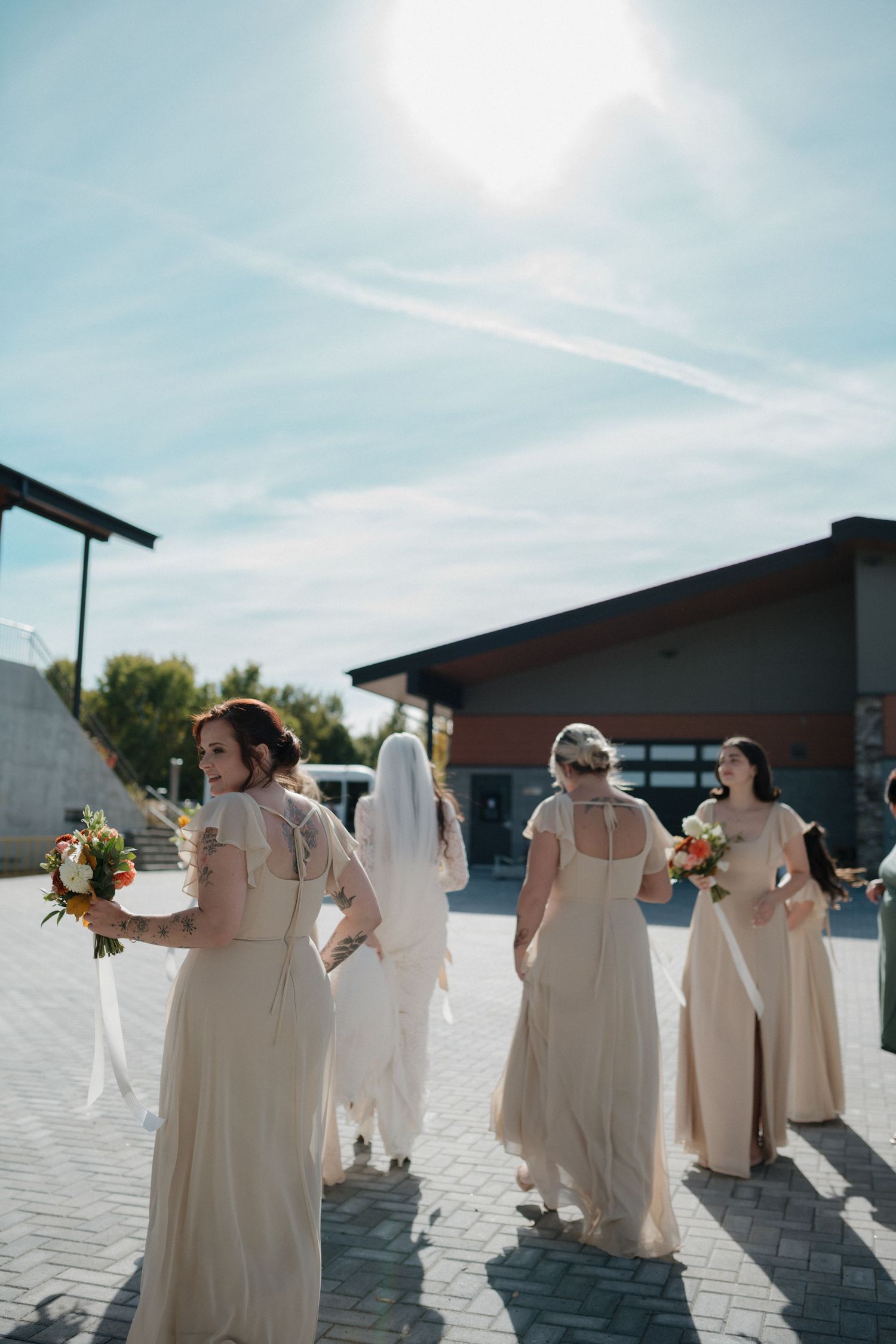 Bridesmaids in blush dresses walking outdoors on a sunny day.