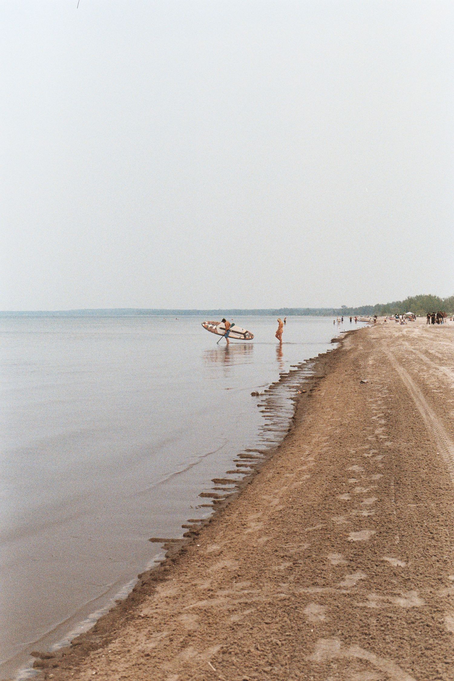 People enjoying a peaceful day at a sandy beach with calm waters and wooden breakwater barriers along the shoreline.