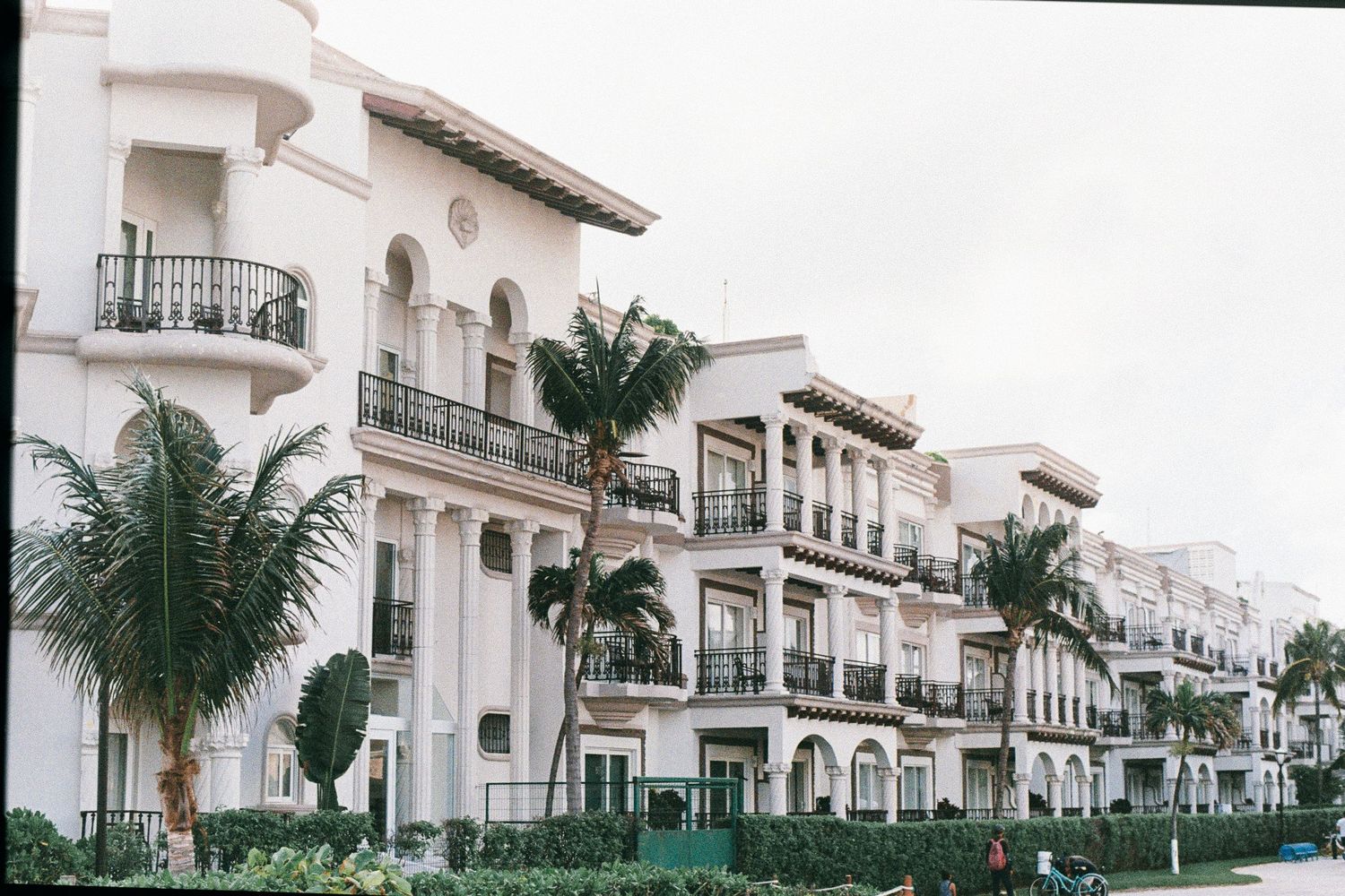 White Mediterranean-style beachfront condominiums with palm trees and balconies.
