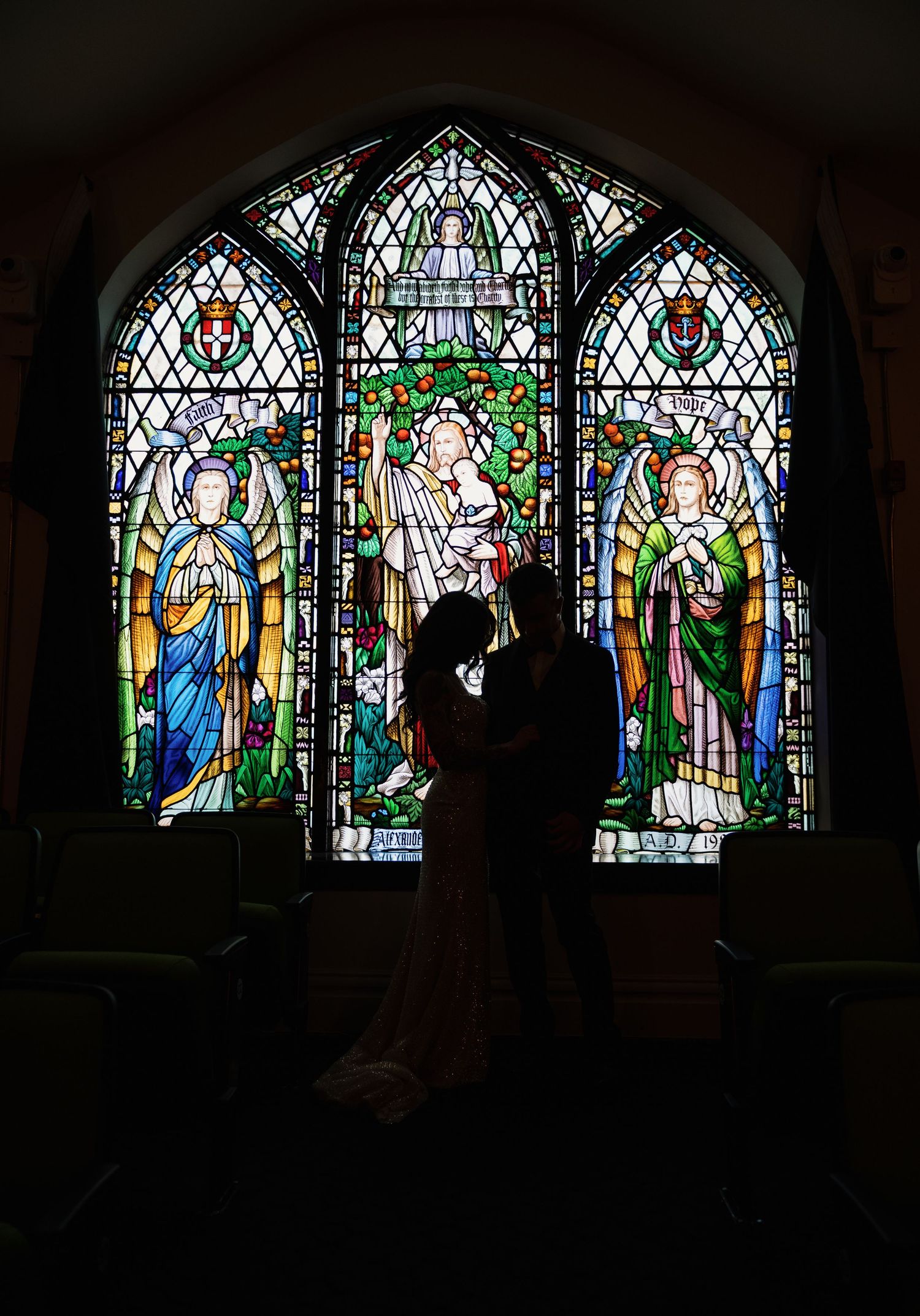 Silhouette of a couple sharing a romantic moment in front of a stunning stained glass window in a church.
