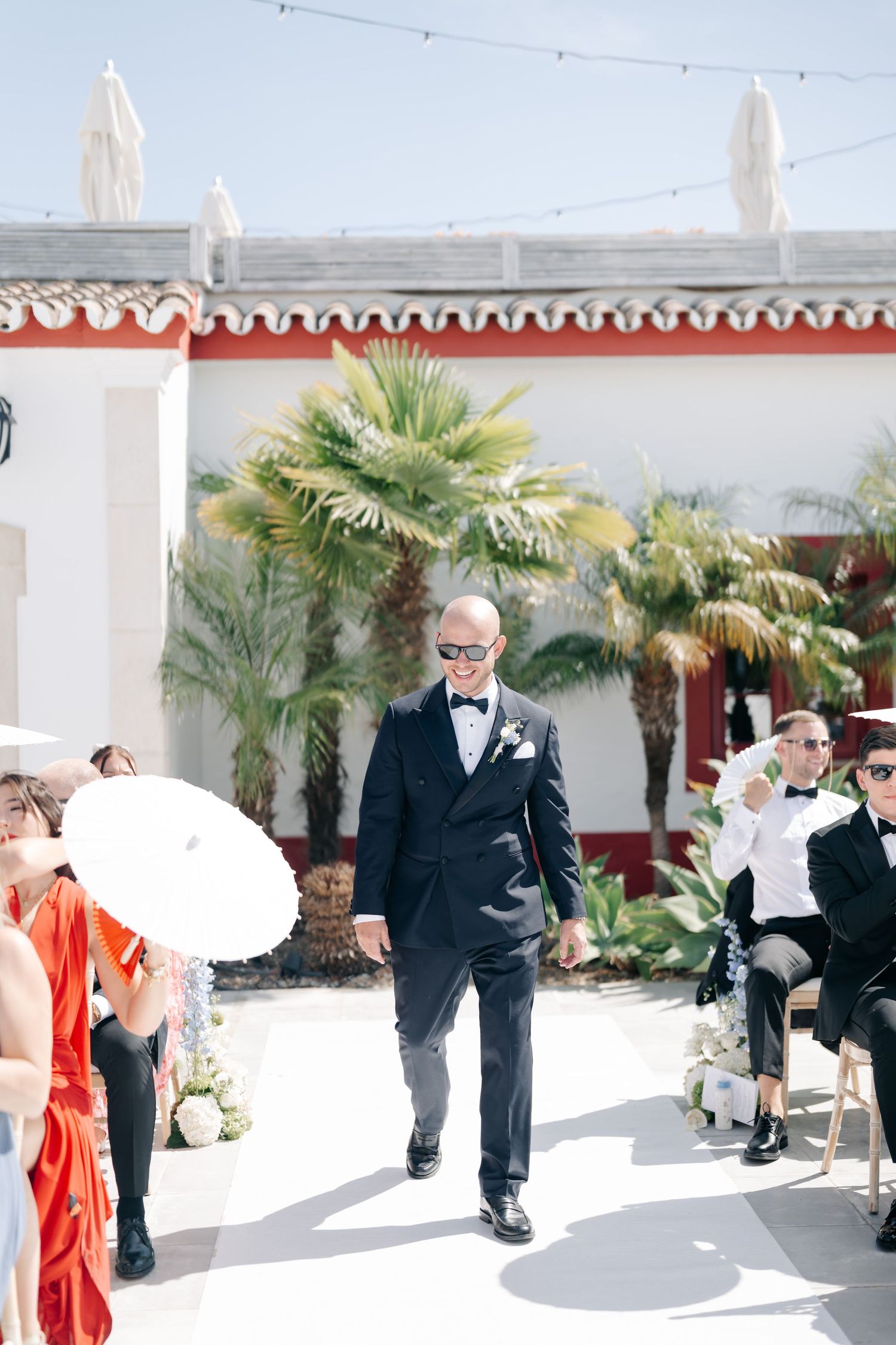 Outdoor wedding ceremony setup with palm trees and white decor at a sunny venue.