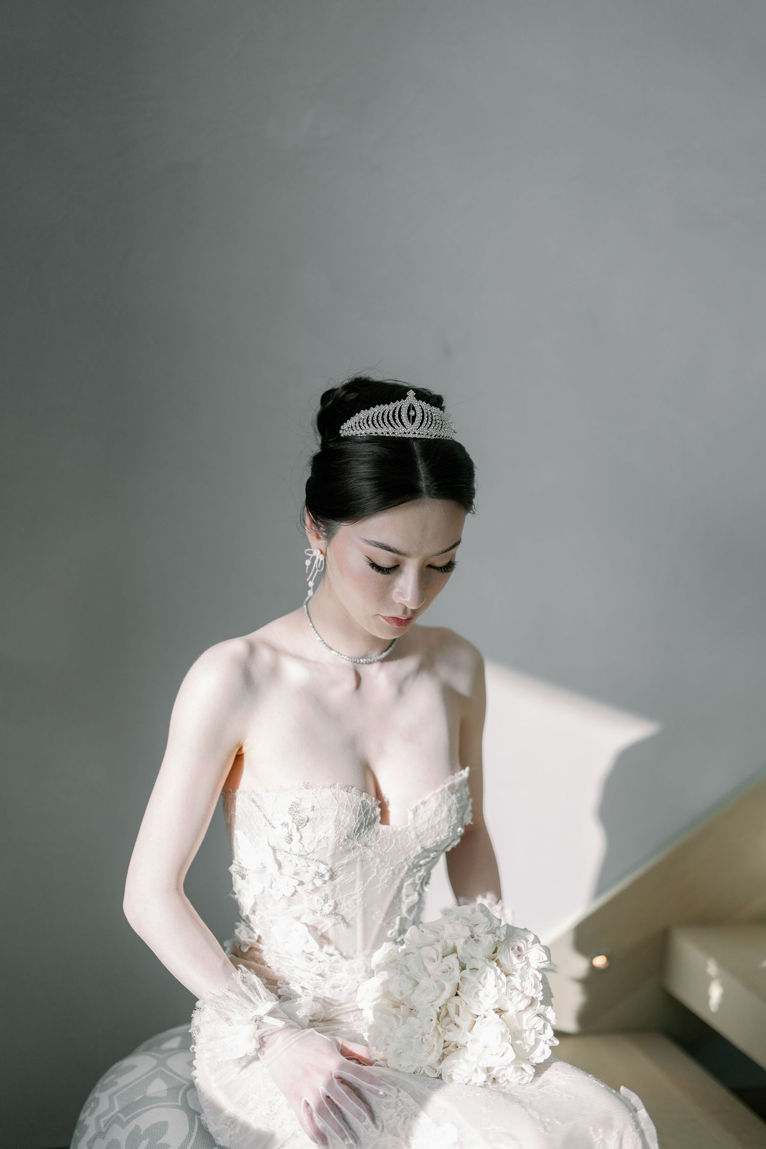 Elegant bridal portrait with lace gown and tiara against grey background.