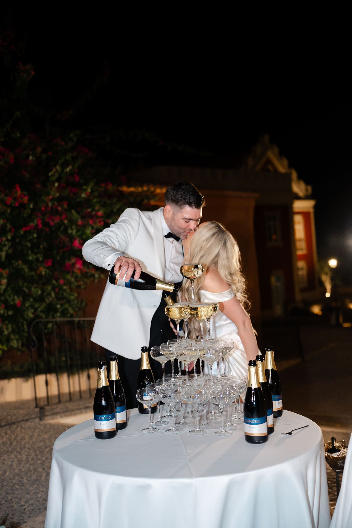 Couple pouring champagne into stacked glasses during wedding celebration.