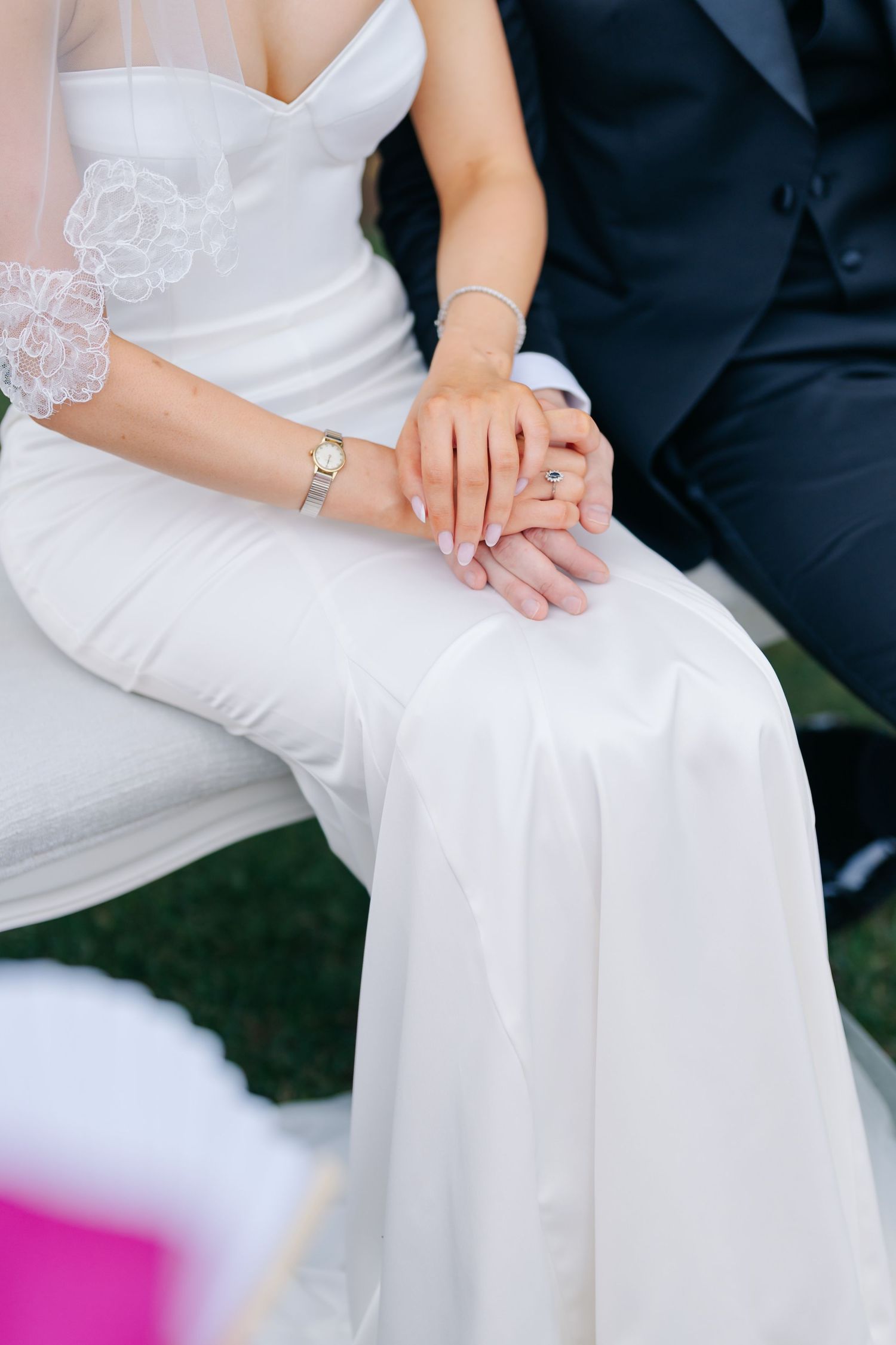 Close-up details of a bride's white wedding gown and hands during an outdoor ceremony.