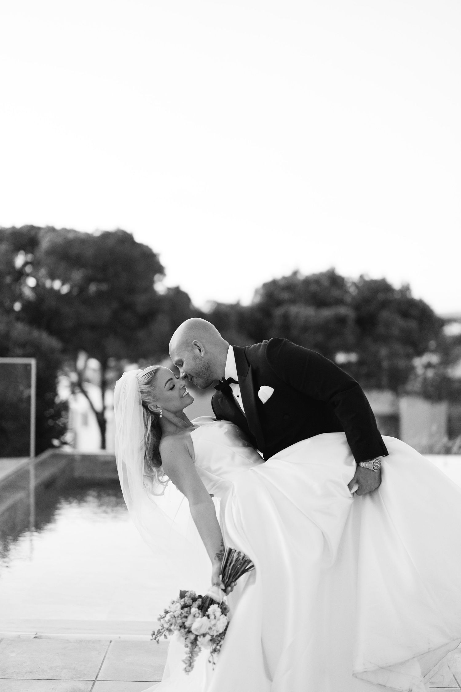 Black and white romantic wedding photo showing couple in intimate moment outdoors.